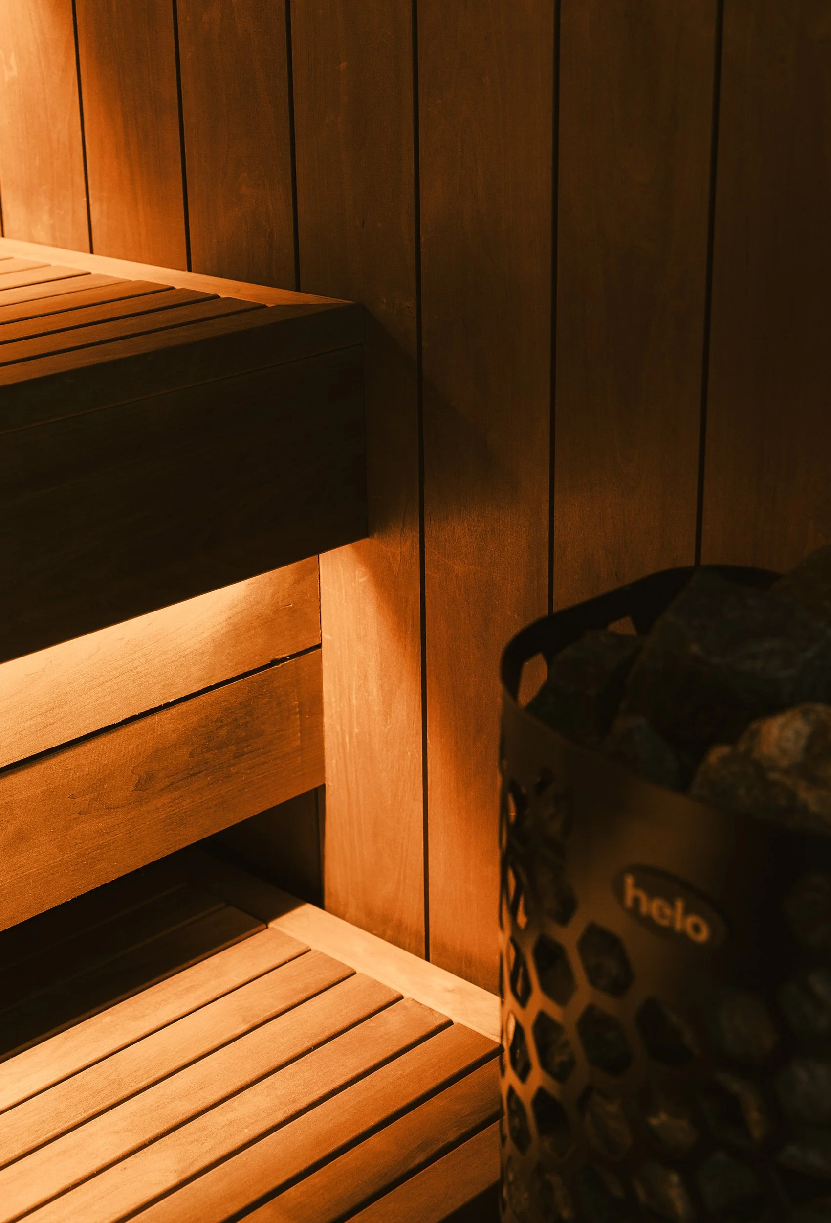 Detalj av badstuebenk, trepanel og integrert belysning ved badstuovnen.