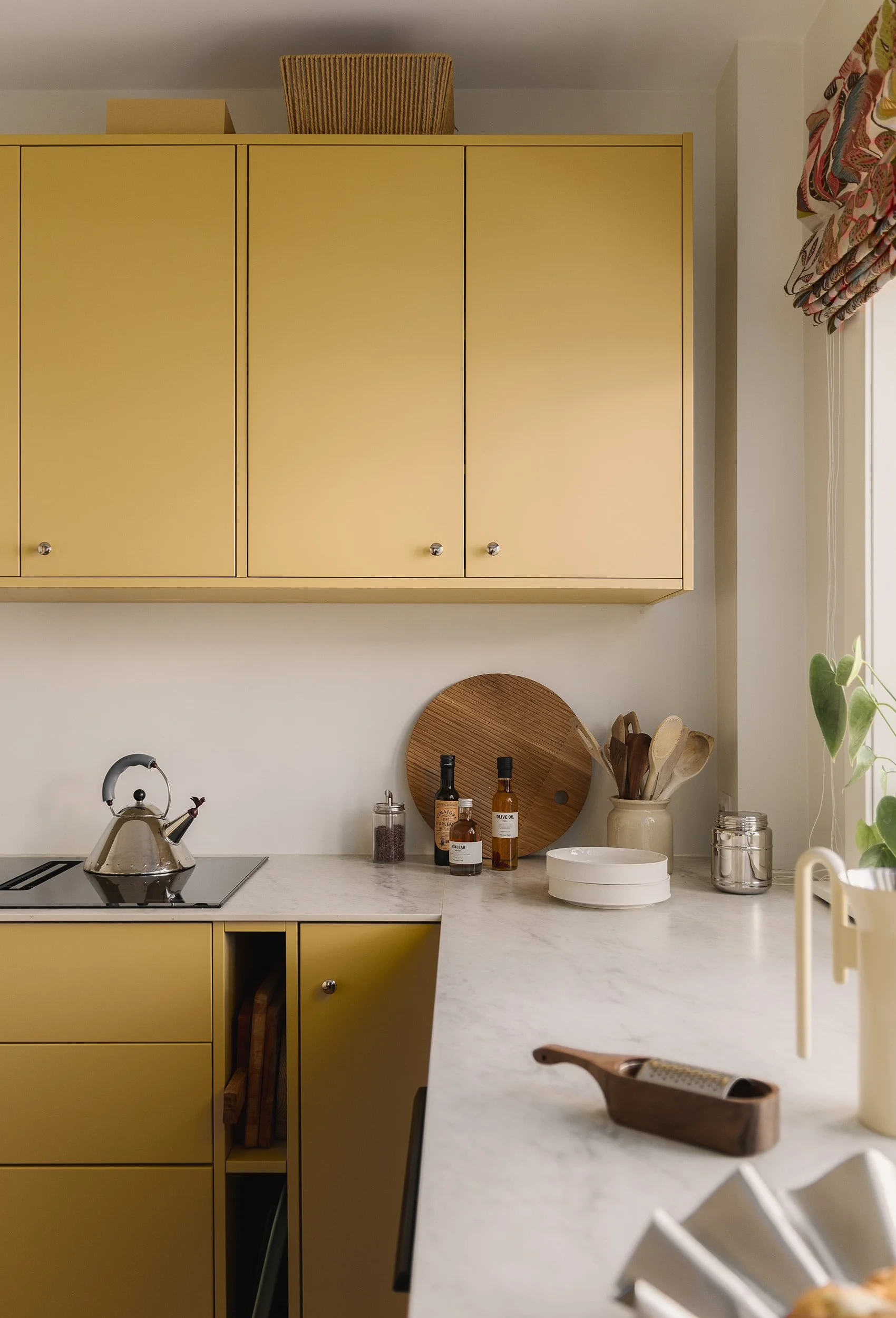 Detalj av gult kjøkken med lys steinbenkeplate og integrert oppbevaring.