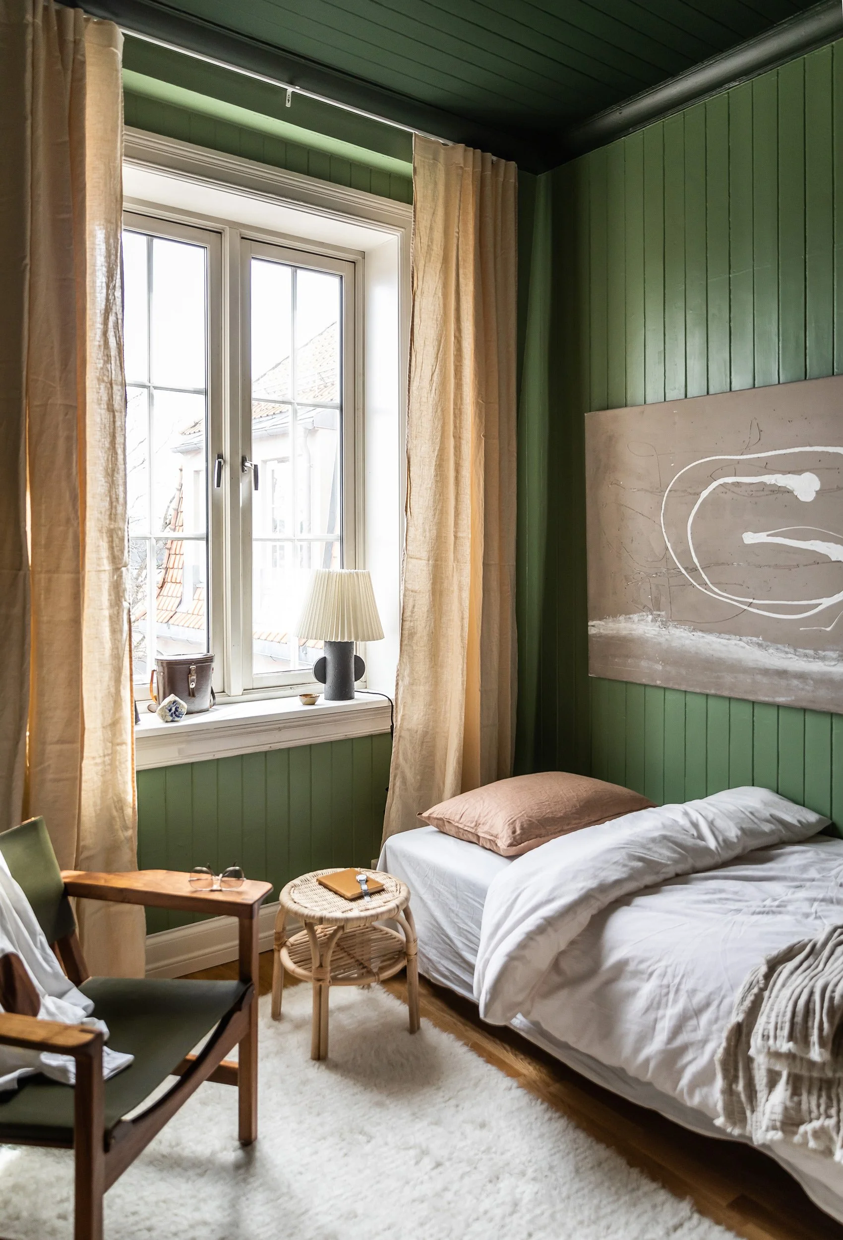 Soverom med mørkegrønt panel på vegger og tak og lyse naturtekstiler.