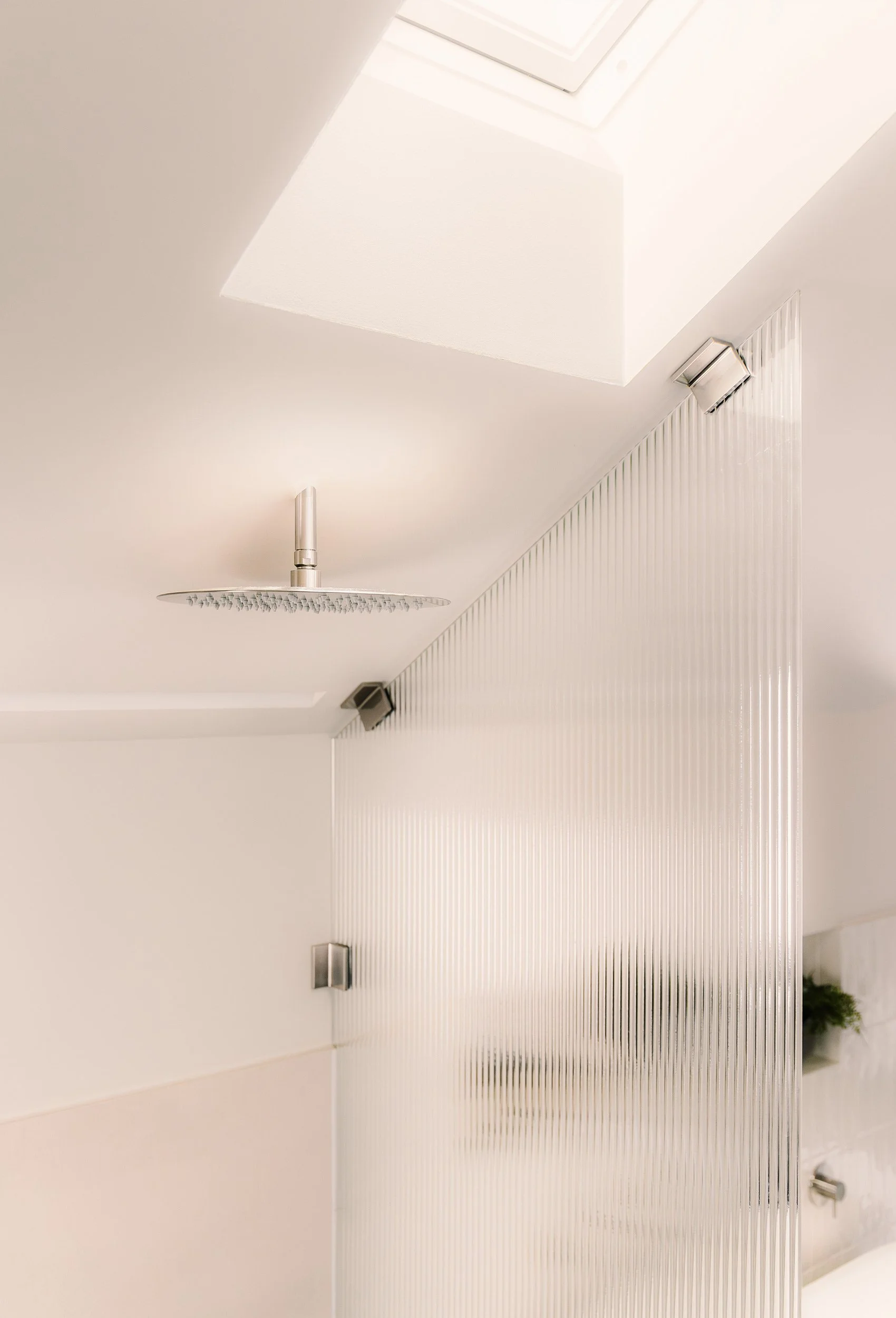 Takvindu over dusjsonen med takdusj og rillet glassvegg som skjermer mot resten av badet.