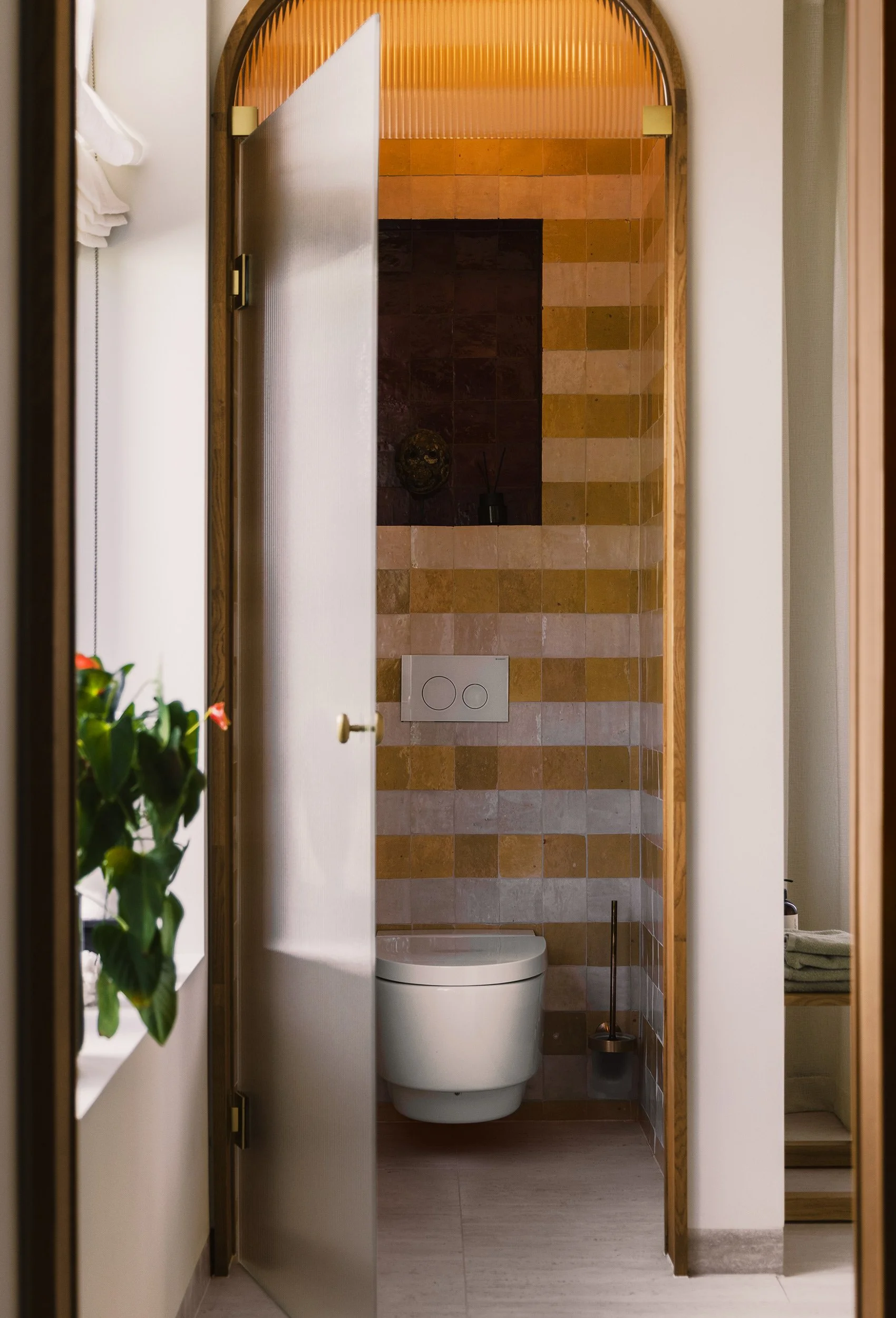 Separat WC i spaavdelingen med buet åpning og håndlagde fliser i varme, varierte toner.