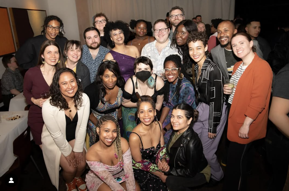 A diverse group of people, including Maria Servellon, at a celebration or social event, smiling and posing for a photo indoors.