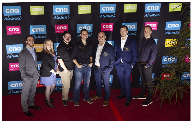 A group of people standing in front of CNA step and repeat.