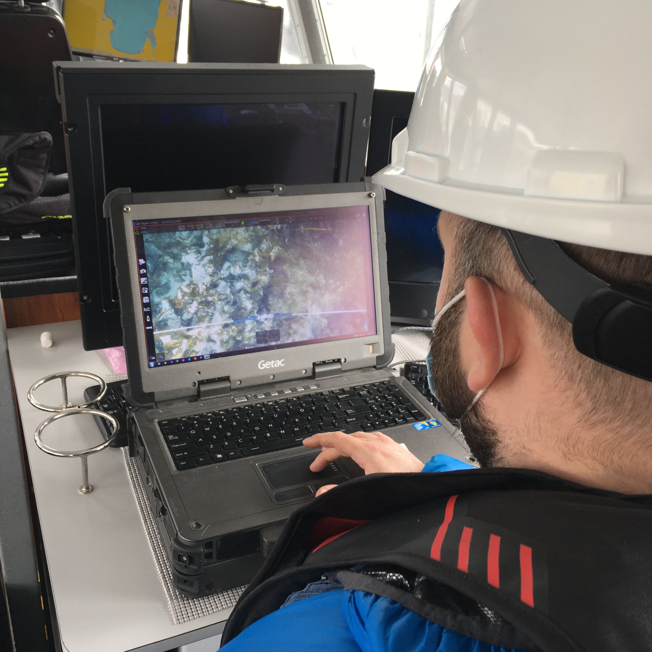 Man with hardhat looks at computer screen showing underwater video