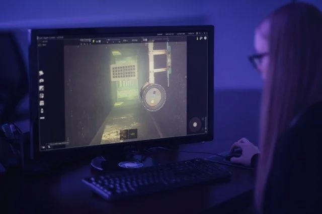 A woman at a computer looking at a image underwater on the screen.