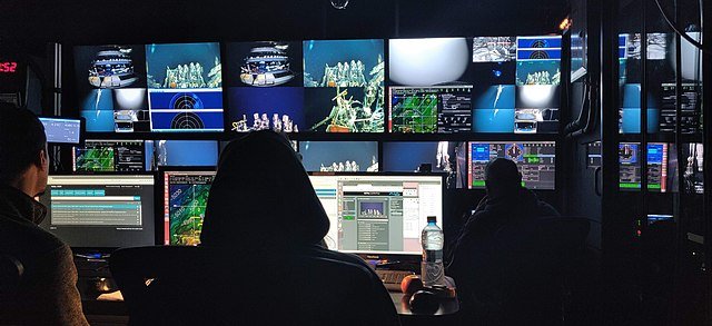 People in dark room looking at screens of subsea remote operations.