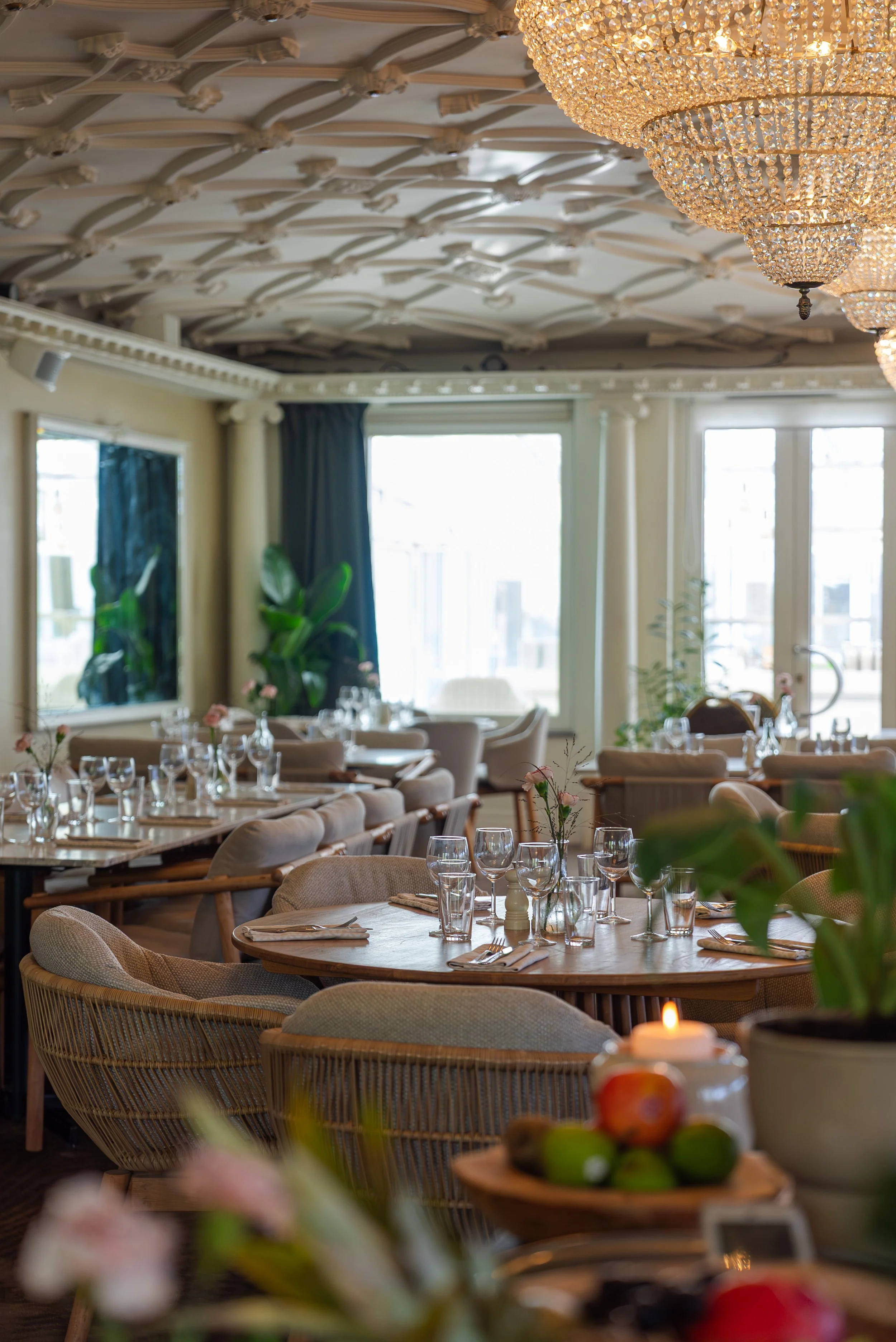 Borda dekorerad med ett ljus i en ljusstake, en vit ros, och ett antal glas med olika drycker, inklusive champagne och rödvin, samt tallrikar med mat såsom sallad, charkuterier, en hamburgare, och andra små rätter på ett dukat bord.