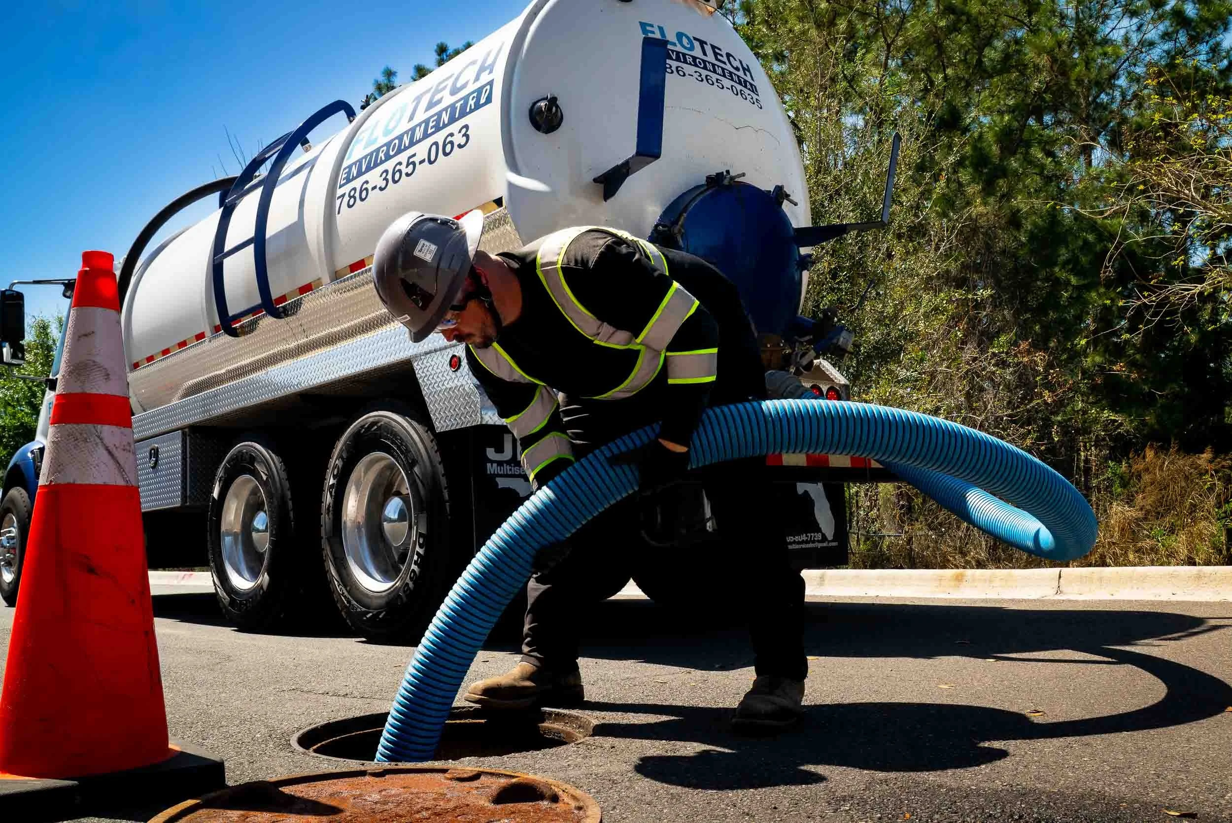 Flow of liquid being poured into a large rusted metal pipe underground, with a nearby metal grate and structural supports.