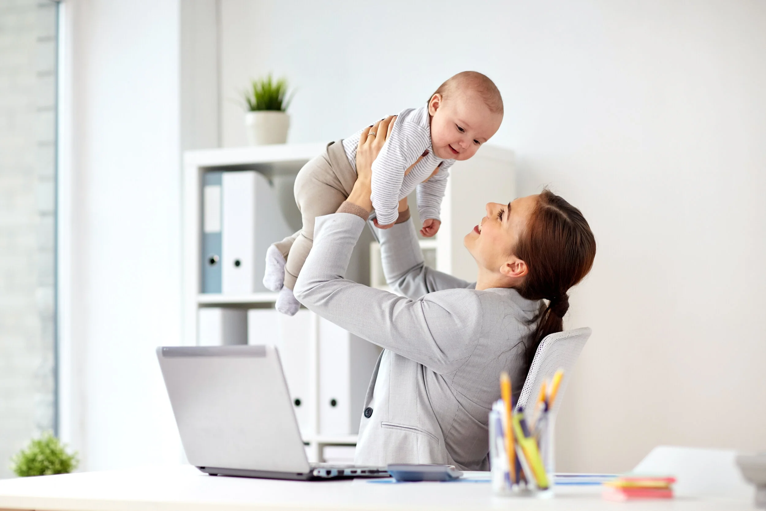 happy-businesswoman-with-baby-and-laptop-at-office-P2DZCUW.jpg