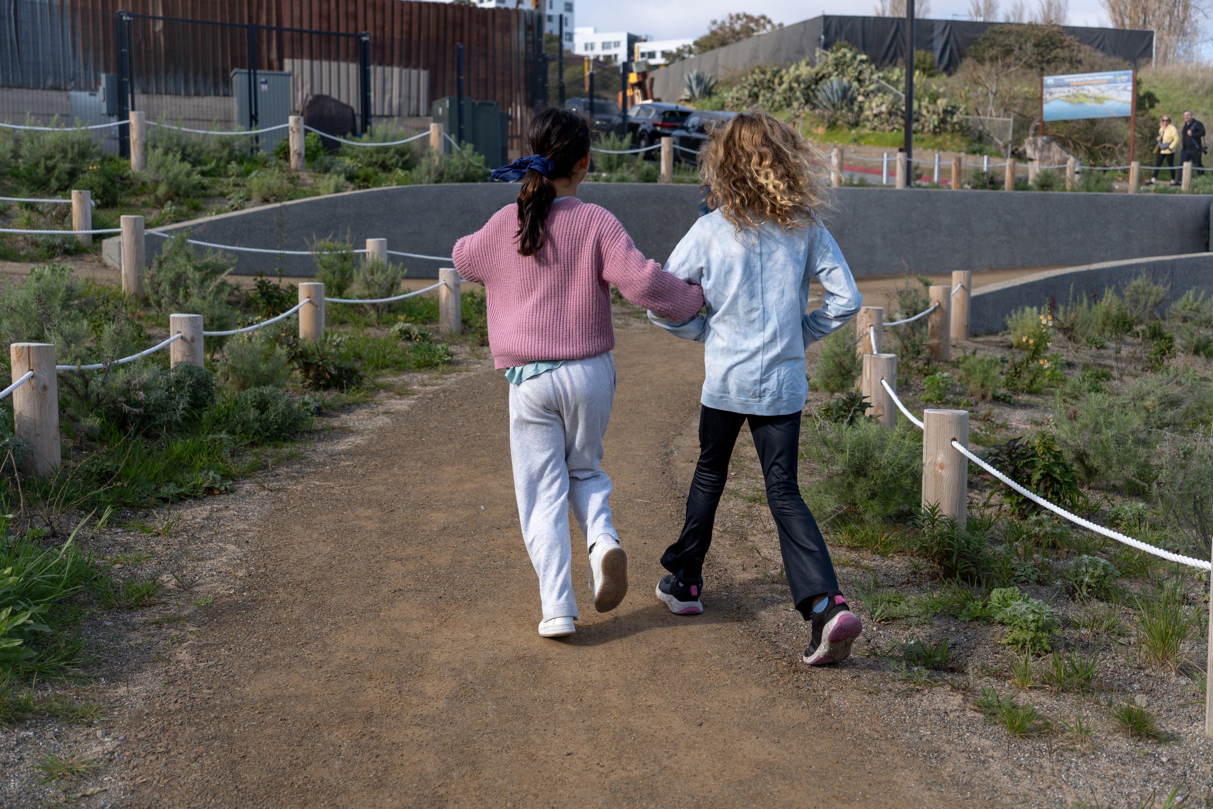 Two young girls skipping along a trail, walking away from the camera. Photo by Mia Candy.