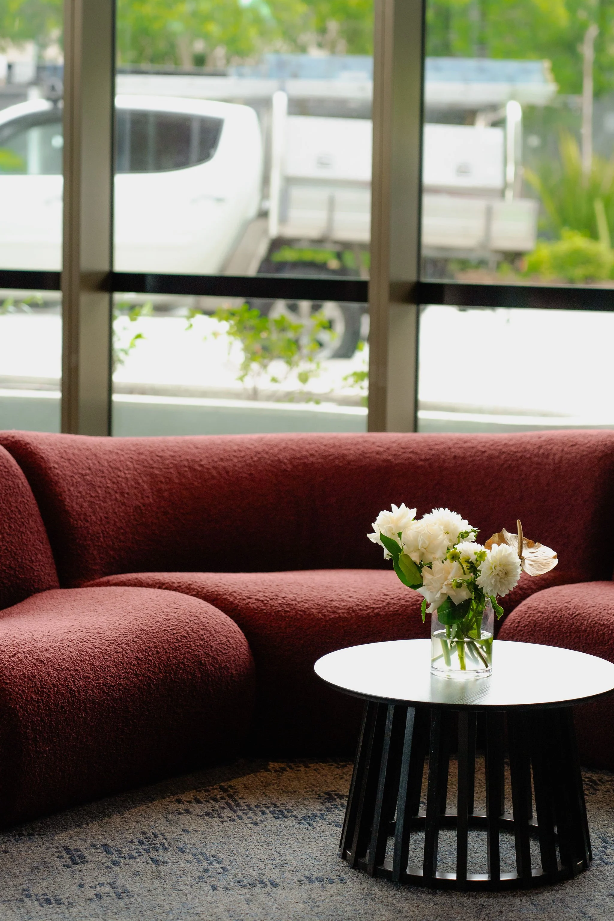 Luxury curved modular lounge in deep red fabric styled in a modern Sydney venue with floor-to-ceiling windows, available for premium event furniture hire by HYRE EVENTS.
