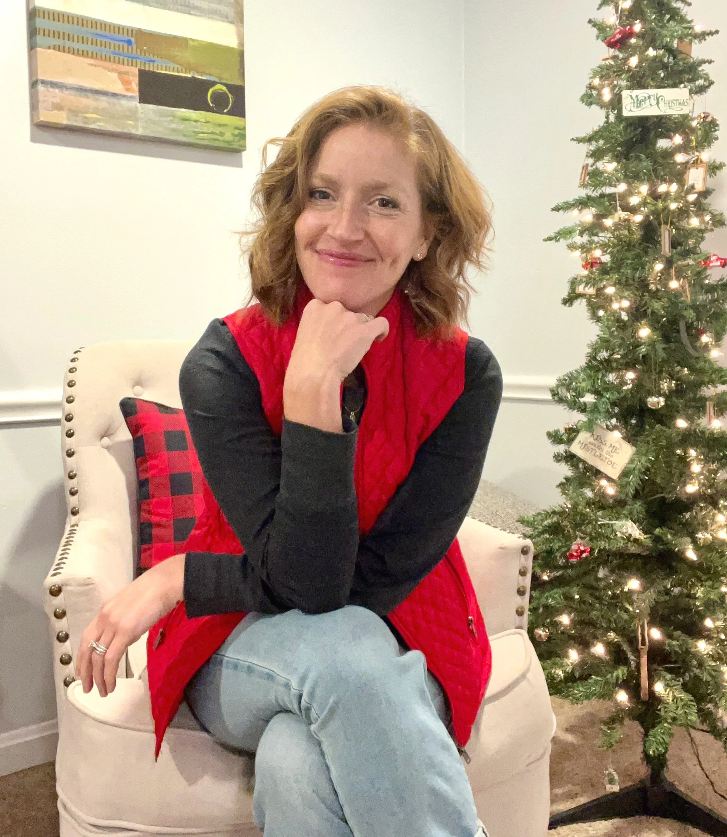 Author Jen Craven seated next to a Christmas tree.