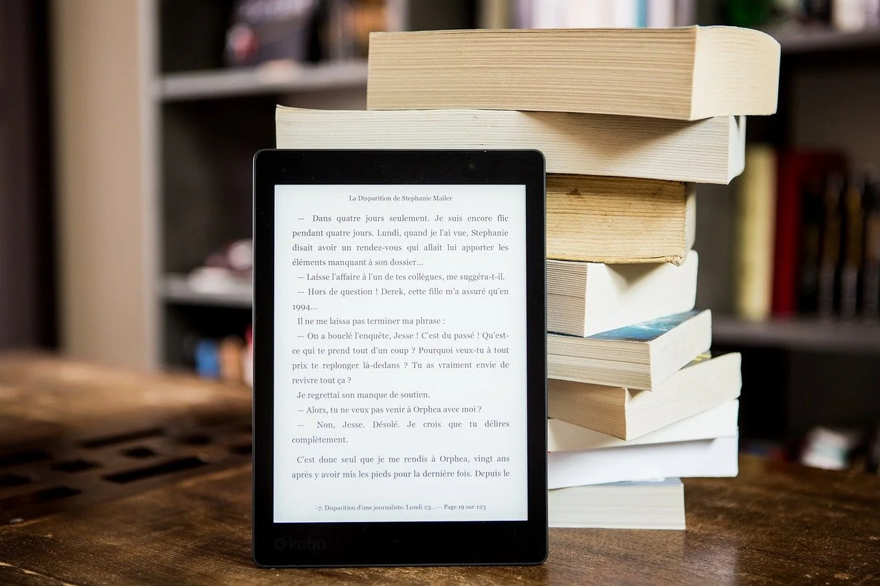 An e-book reader propped up against a stack of paperback books.
