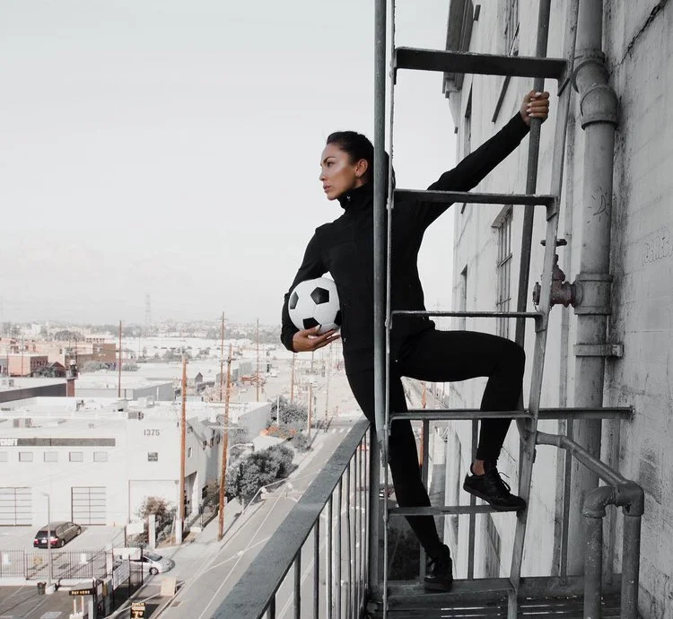 woman looking out on a ladder while holding a soccer ball