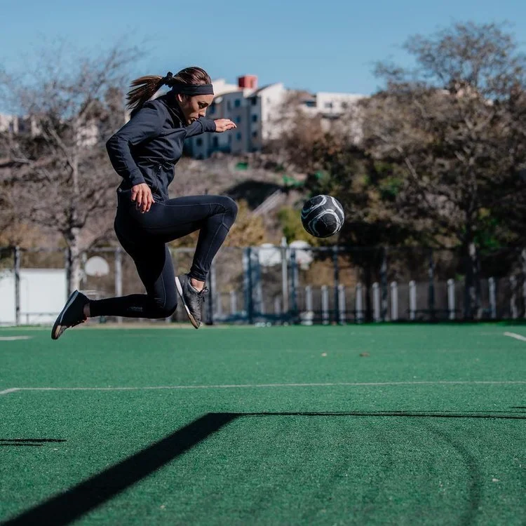 Woman jumping in the air on soccer field with soccer ball