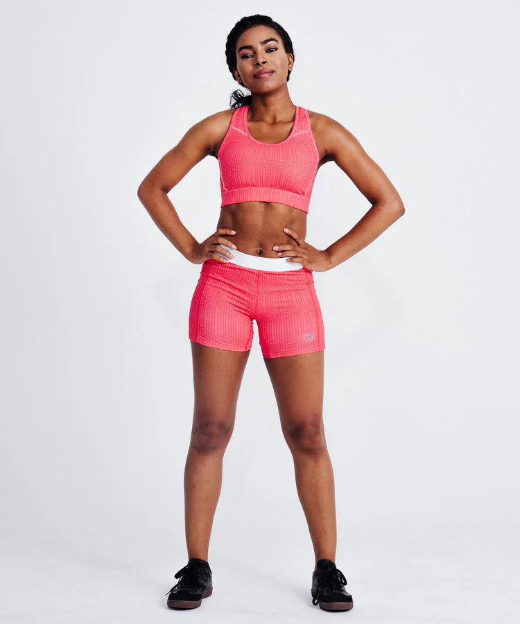 Woman standing in front of white background wearing a pink workout set