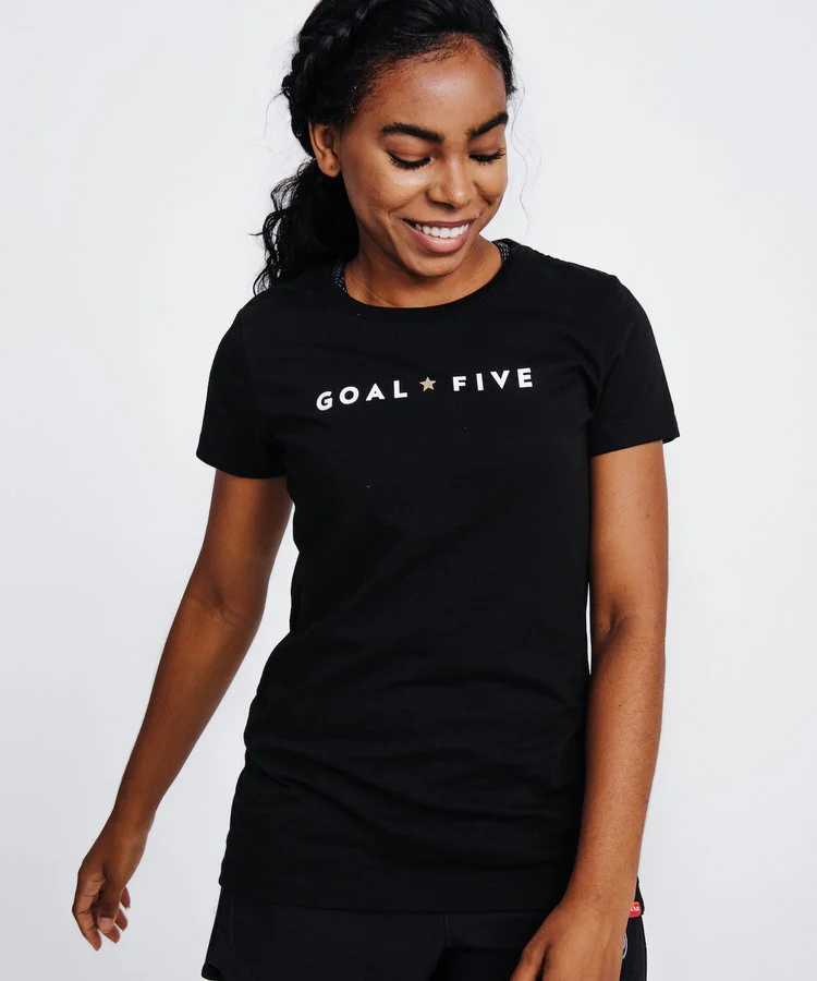 Woman standing in front of white background wearing a Goal Five shirt