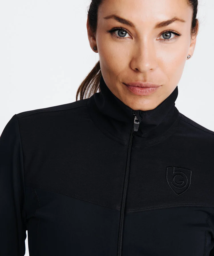 Woman standing in front of white background wearing a black zip up