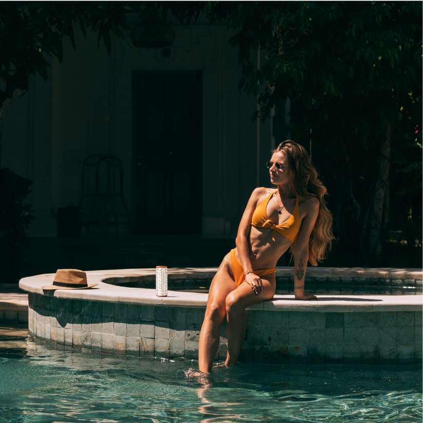Woman sitting by the pool with a Decada can