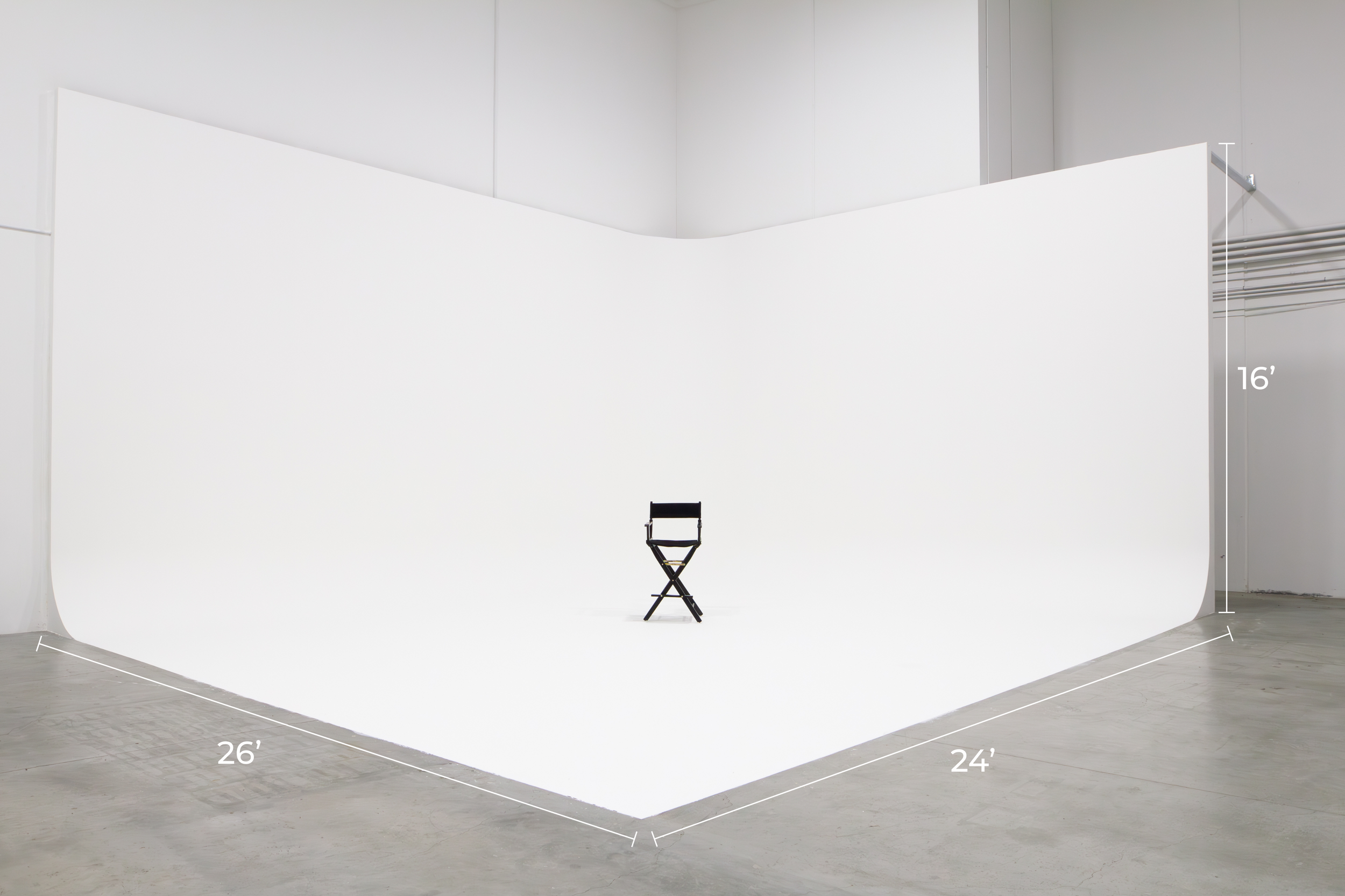 A black folding chair placed in the center of a white photography studio backdrop, measuring 26 feet wide and 24 feet deep, with a height of 16 feet. ONA Studios.