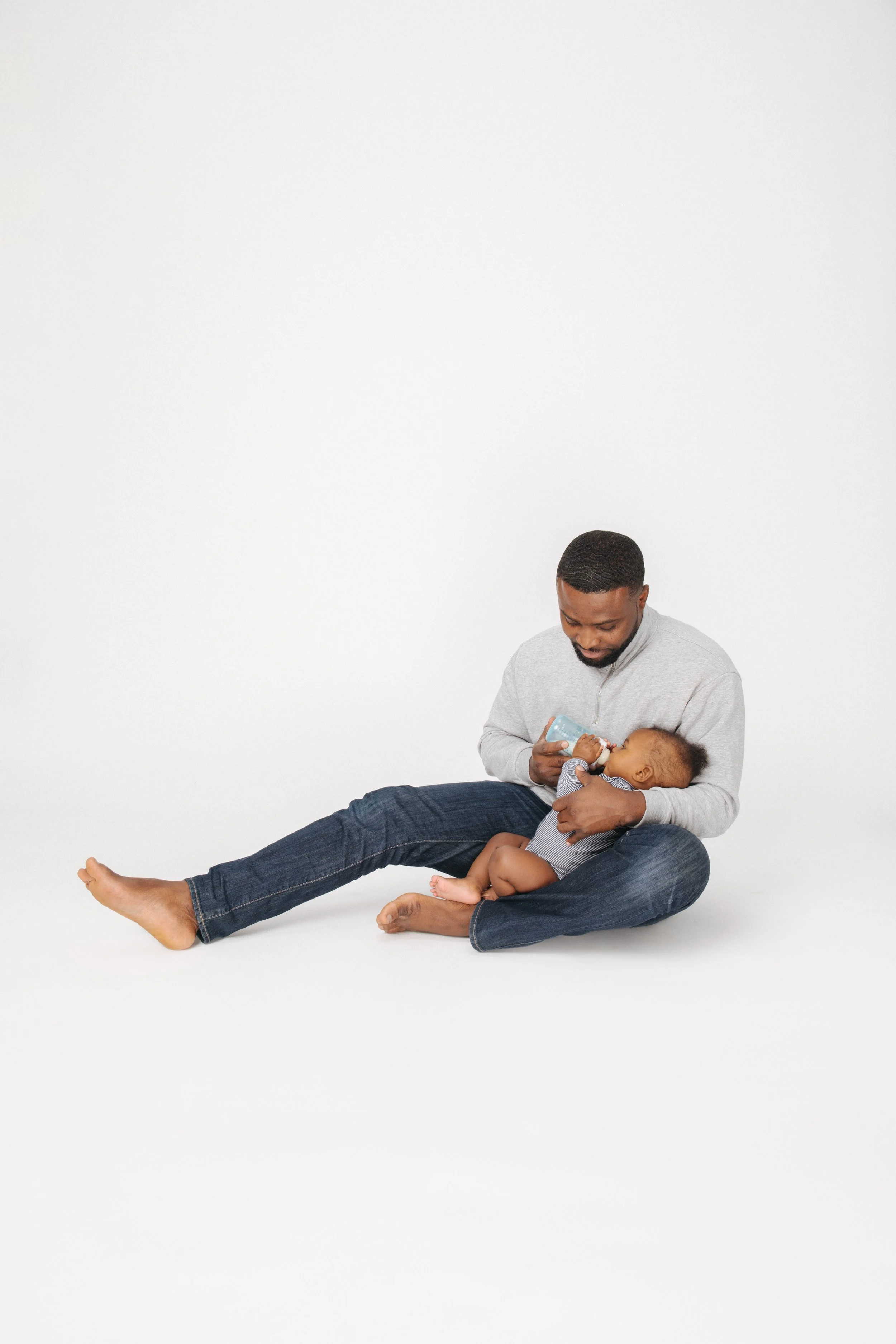 Dad feeding baby on the ground in front of white background