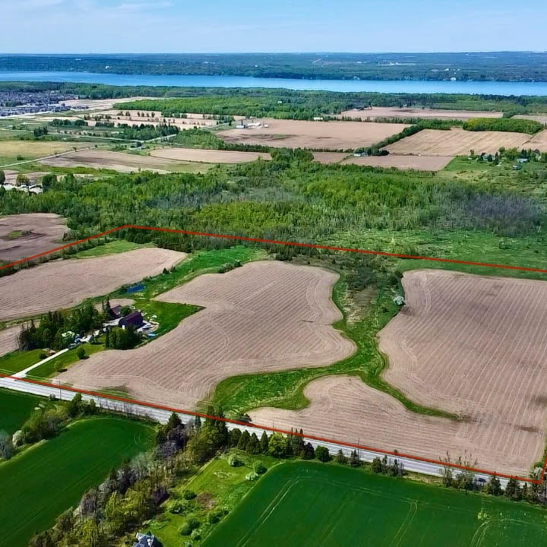 Aerial view of farmland with patches of green and brown fields, a river in the background, and a forested area near the center.