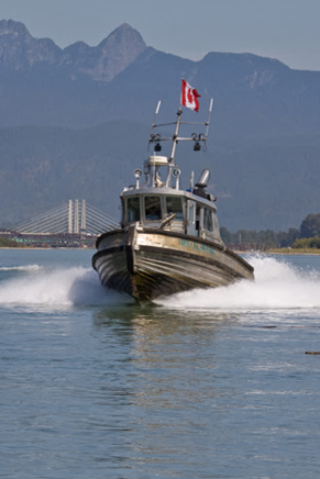 A boat with a Canadian flag sailing on water near mountains and a bridge in the background. KNW Diesel provide installation, sales and service of Marine engines Scania, FPT, Moteurs Baudouin in British Columbia