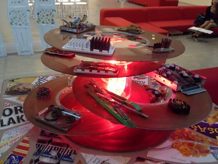 Art installation with spiral design and electronic components on red lighted base, in modern interior setting.