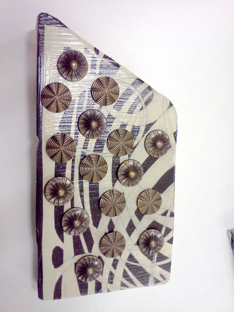 Decorative artwork featuring black and white patterns with circular metallic elements on a flat, triangular surface.