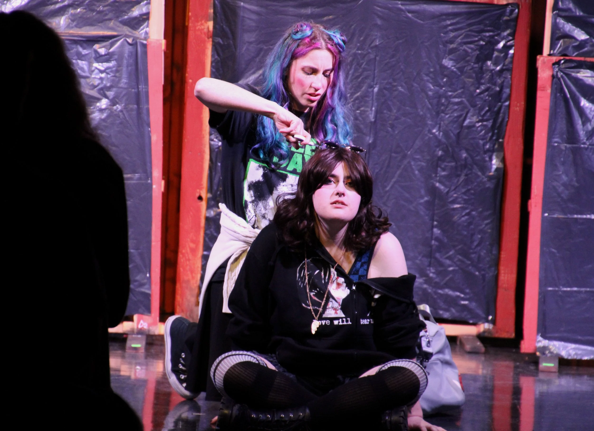 Celia (Evie Bennett) cuts Rosalind (Quinn Trixx)'s hair in order to disguise her for their flight into the woods.