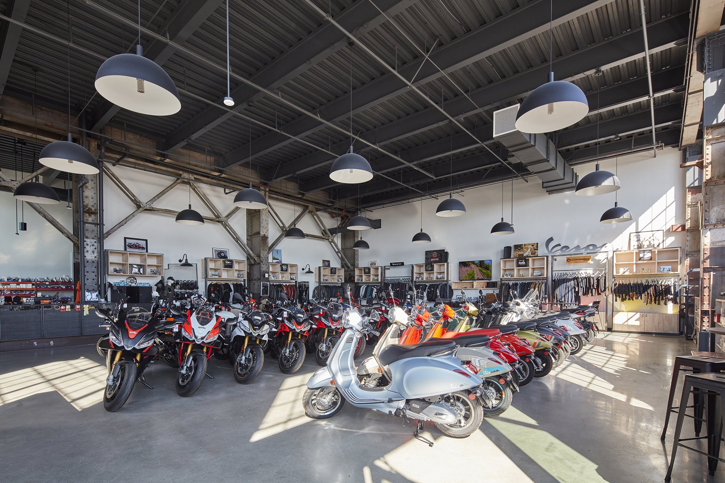 Interior of a motorcycle and scooter showroom with various bikes lined up and merchandise displayed on shelves in the background.