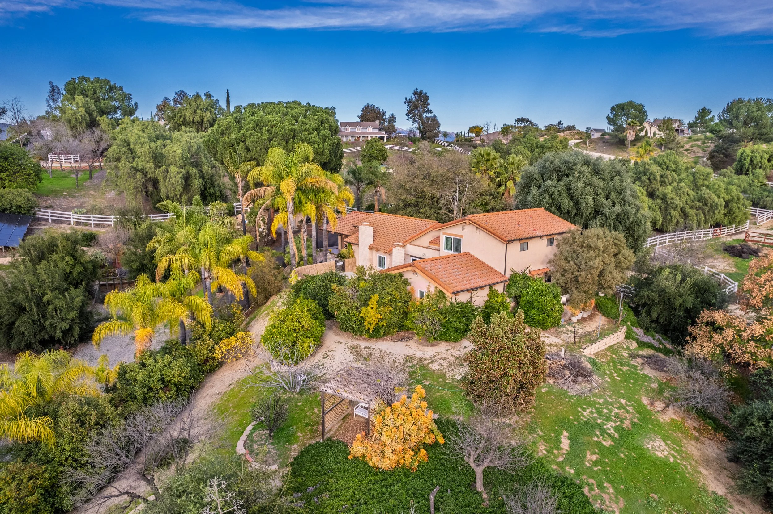 Aerial view of a residential backyard with trees, bushes, and a house with a red tile roof.