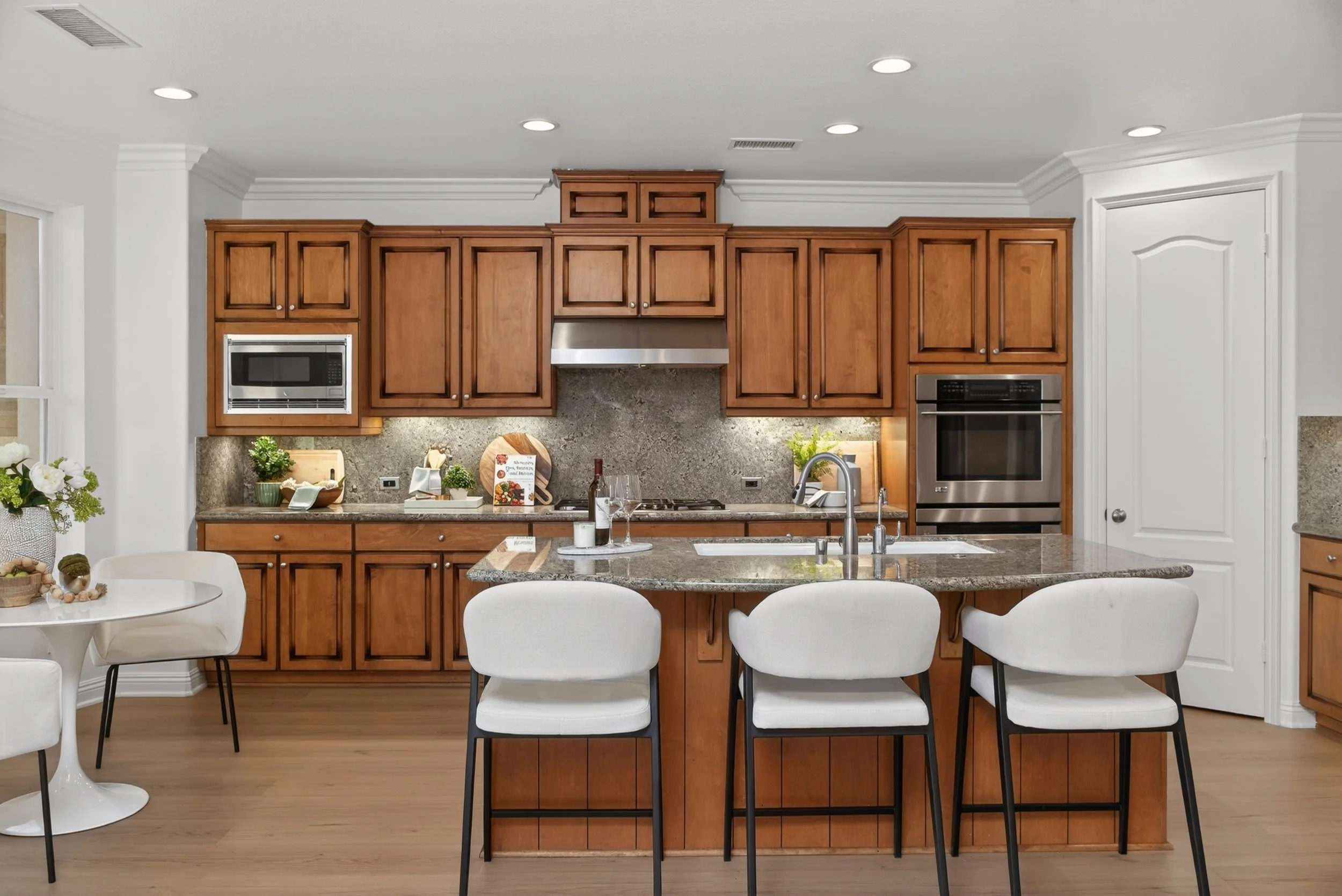 Kitchen with wooden cabinets, stainless steel appliances, a granite island, white chairs, and decorative items on the counters.