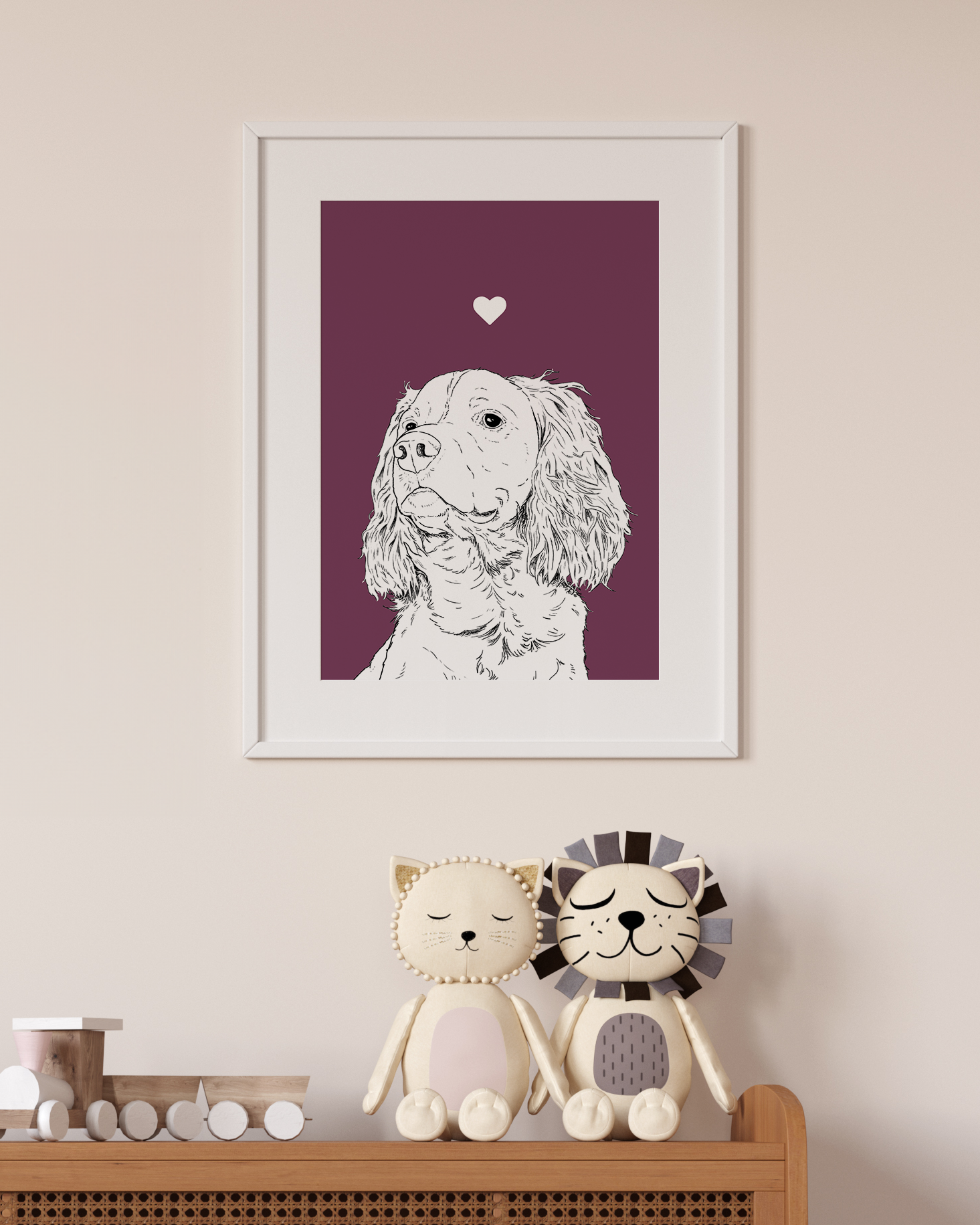 An A4 print in a white frame on a wall above 2 lion toys sitting on a unit. It has a black & white illustration of the head & shoulders of a Springer Spaniel dog on a purple background.