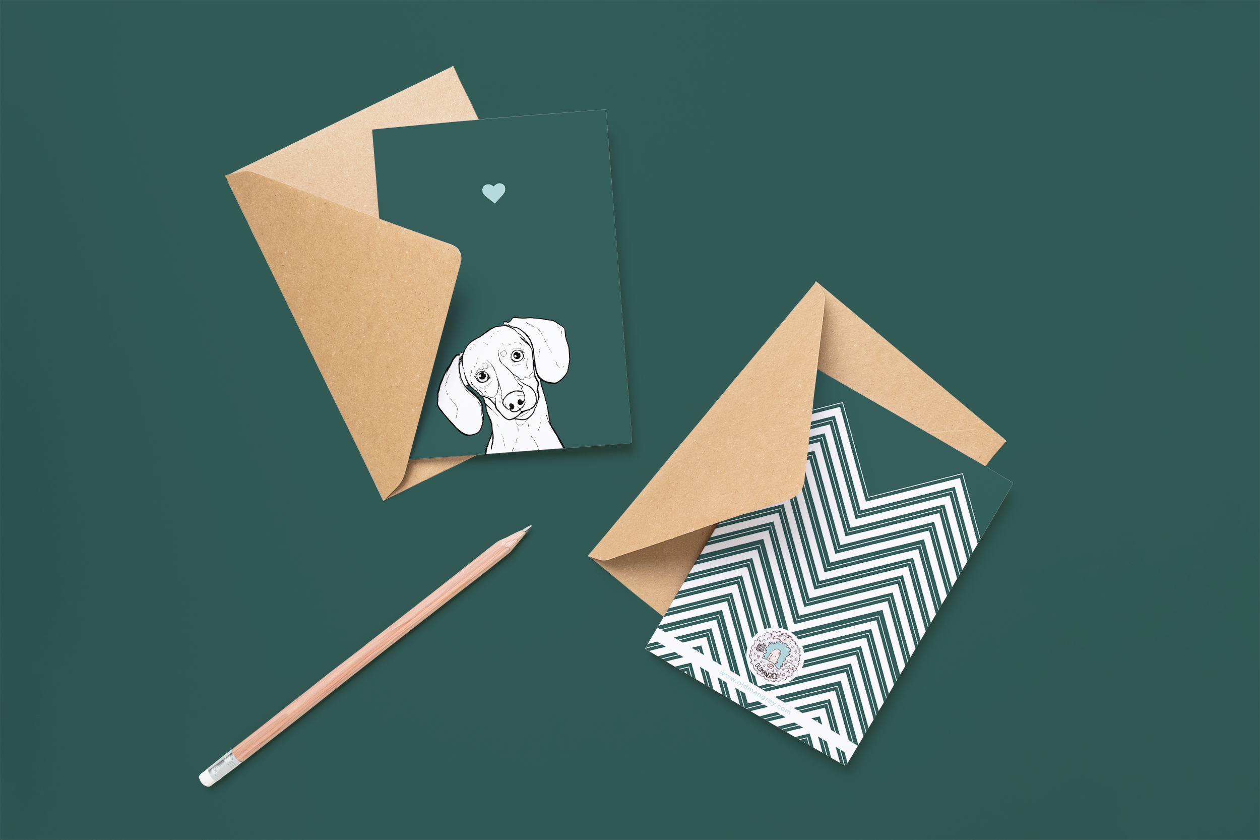 Two cards on brown envelopes, one face up one down. The card and image have a dark green coloured background, with a black & white digital illustration of the head & shoulders of a Mini Dachshund dog.