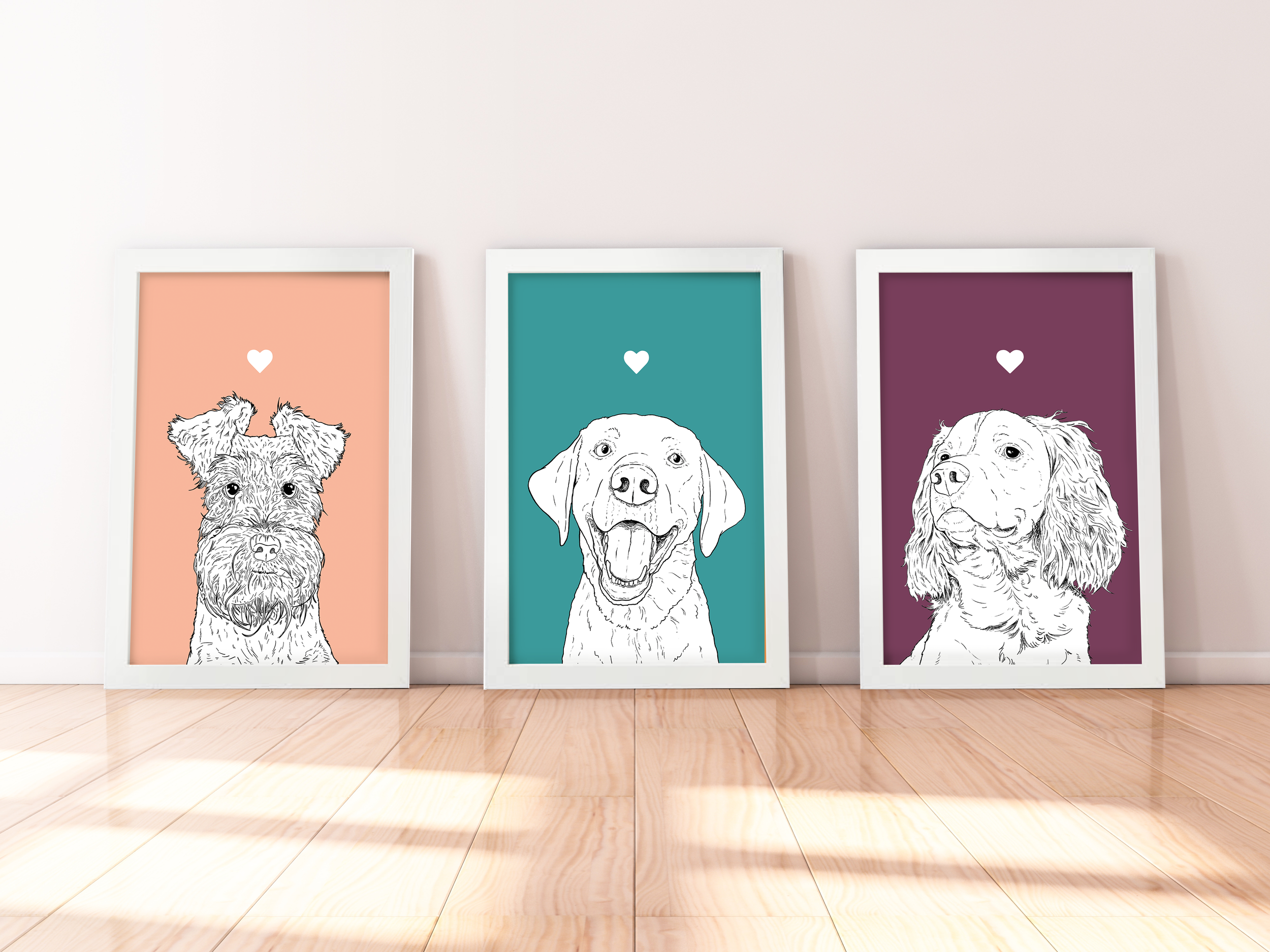 A trio of A4 prints in white wooden frames leaning against a white wall. Each has a black & white digital illustration of the head & shoulders of a different dog breed: Schnauzer, Labrador & Spaniel