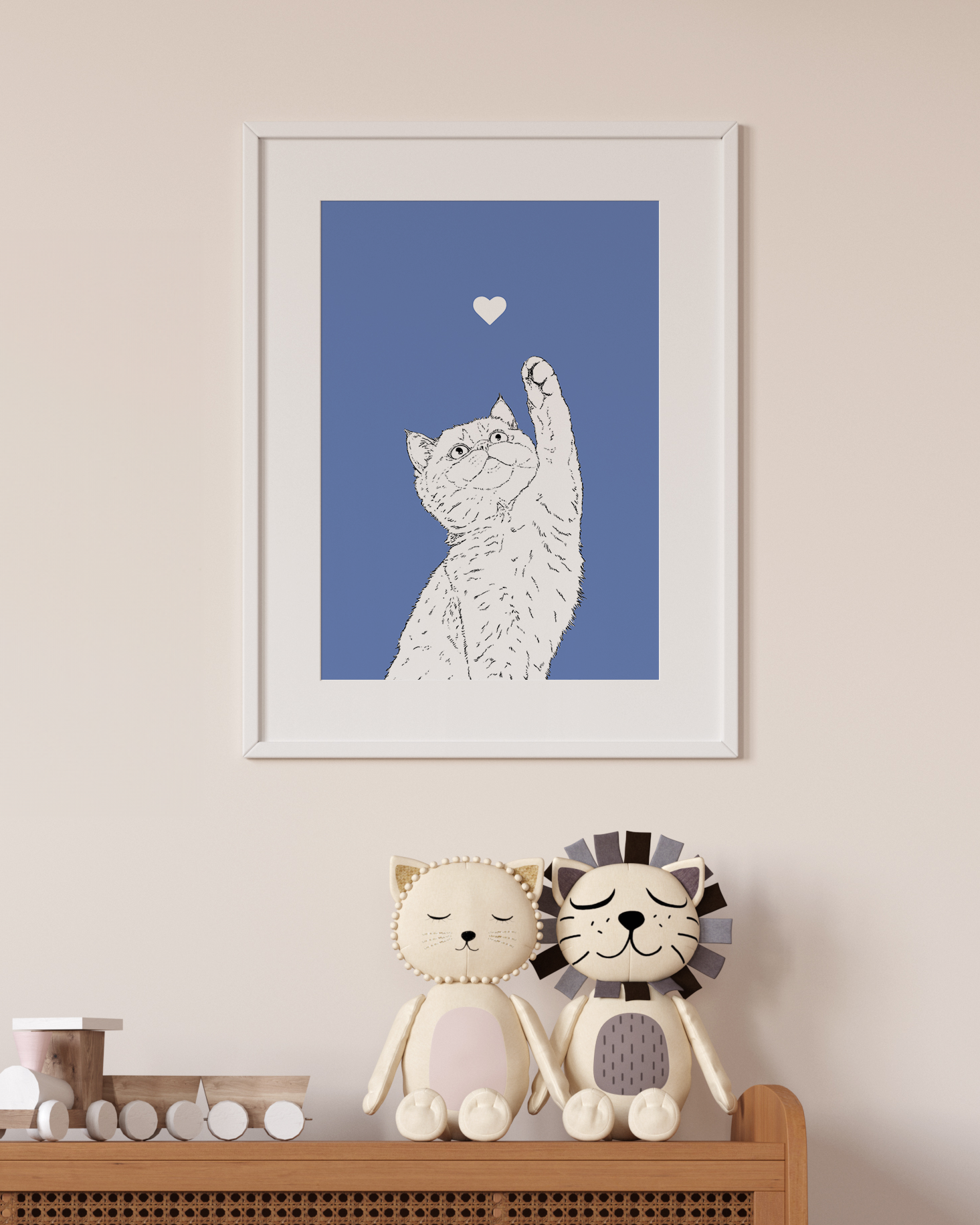 An A4 print in a white frame on a wall above 2 lion toys sitting on a unit. It has a black & white illustration of the head & shoulders of a Kitten on a powder blue background.