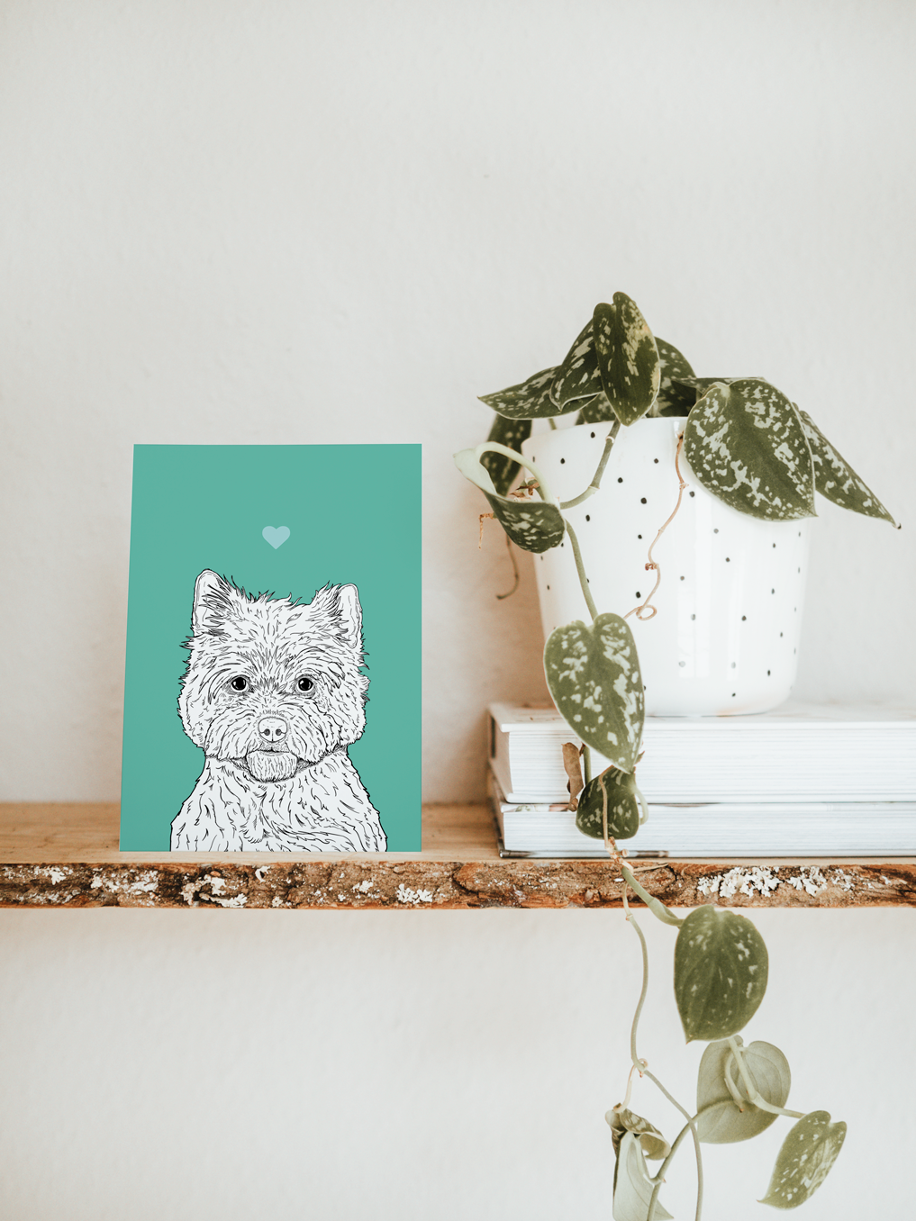 An A6 greetings card & white plant pot on a shelf. The card has a mint green coloured background, with a black & white digital illustration of the head & shoulders of a Cairn Terrier dog.