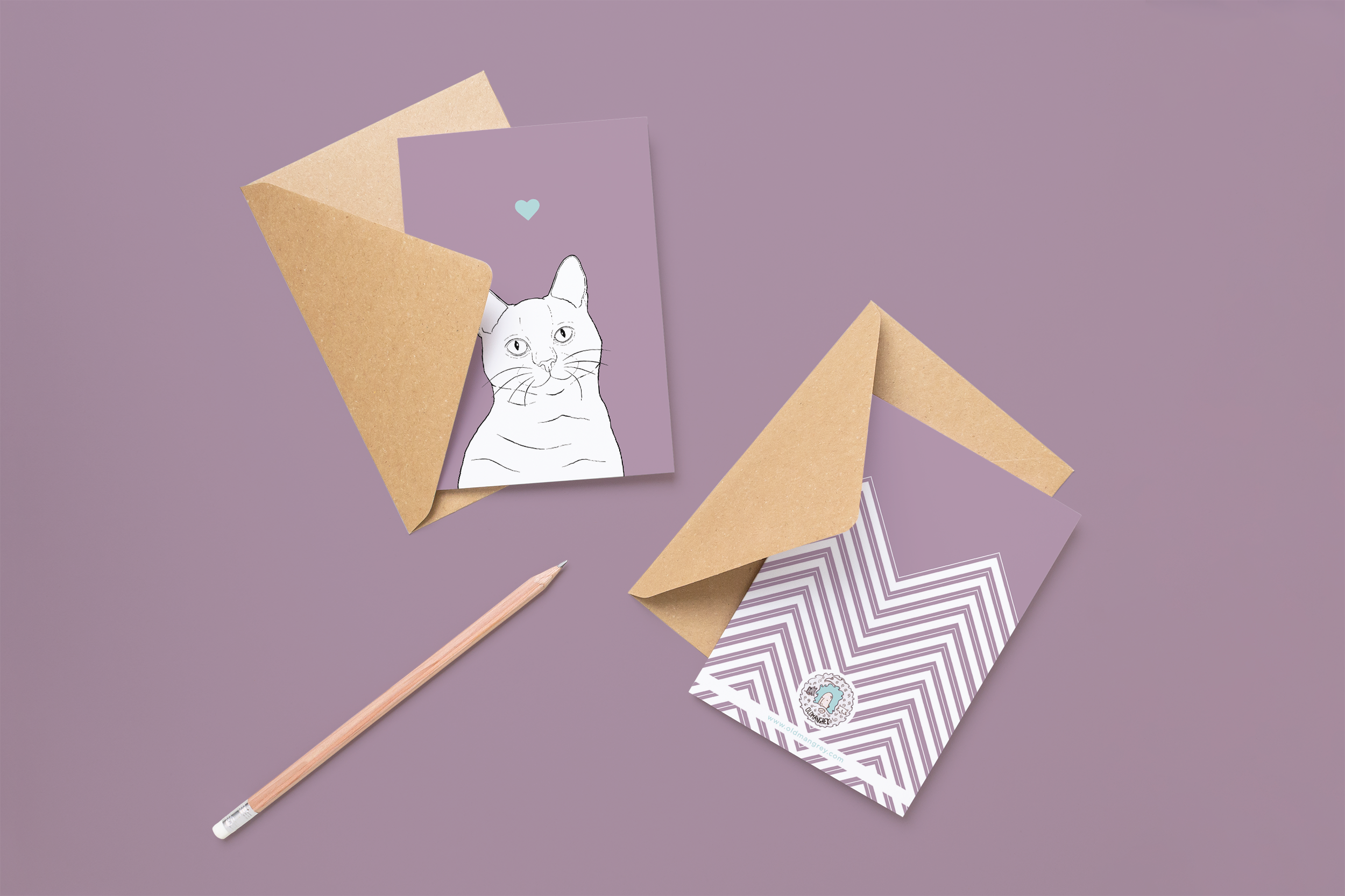 Two cards on brown envelopes, one face up one down. The card and image have a lilac purple coloured background, with a black & white digital illustration of the head & shoulders of a Shorthair cat.