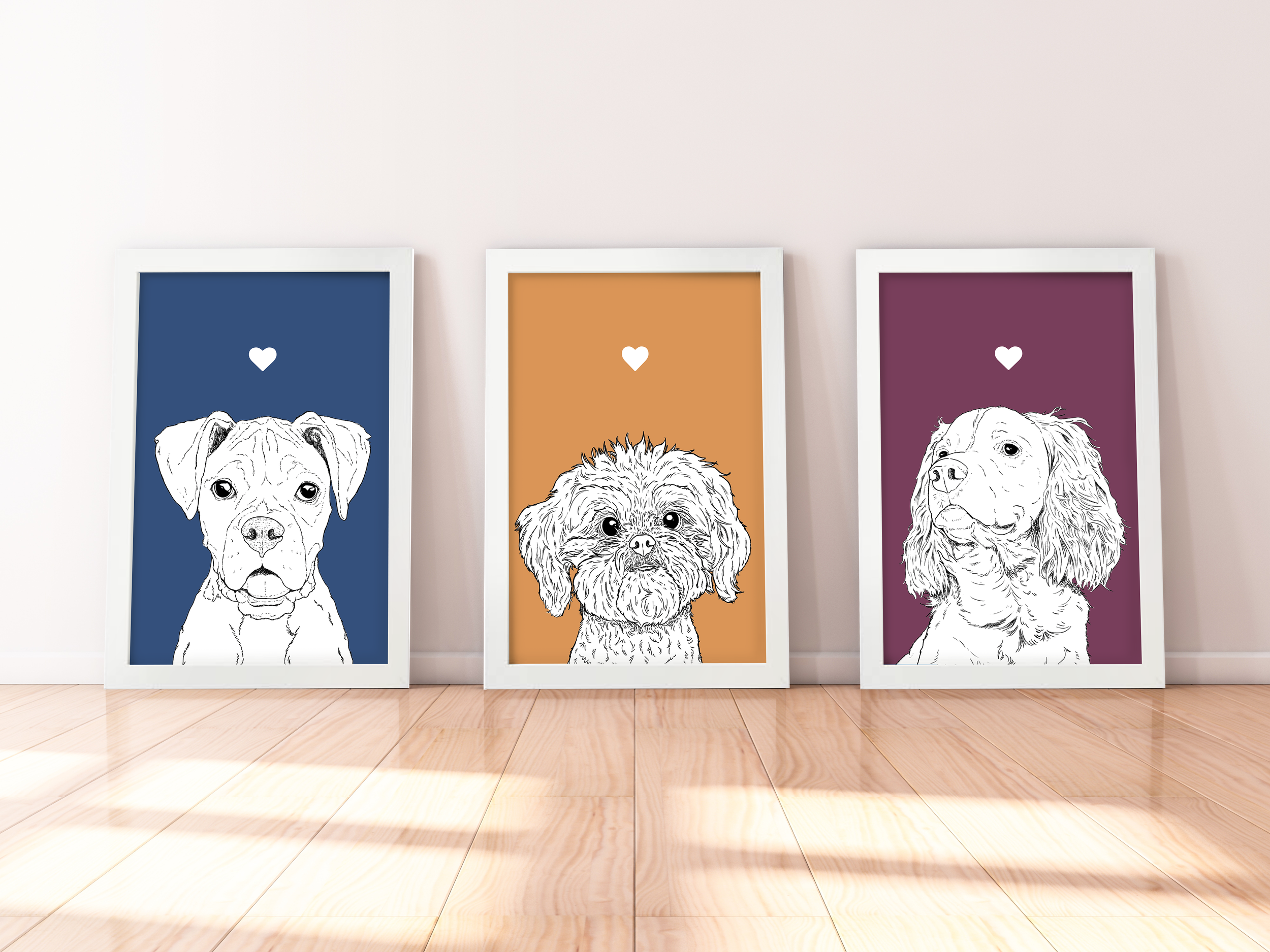 A trio of A4 prints in white wooden frames leaning against a white wall. Each has a black & white digital illustration of the head & shoulders of a different dog breed: Boxer, Shih Tzu & Spaniel.