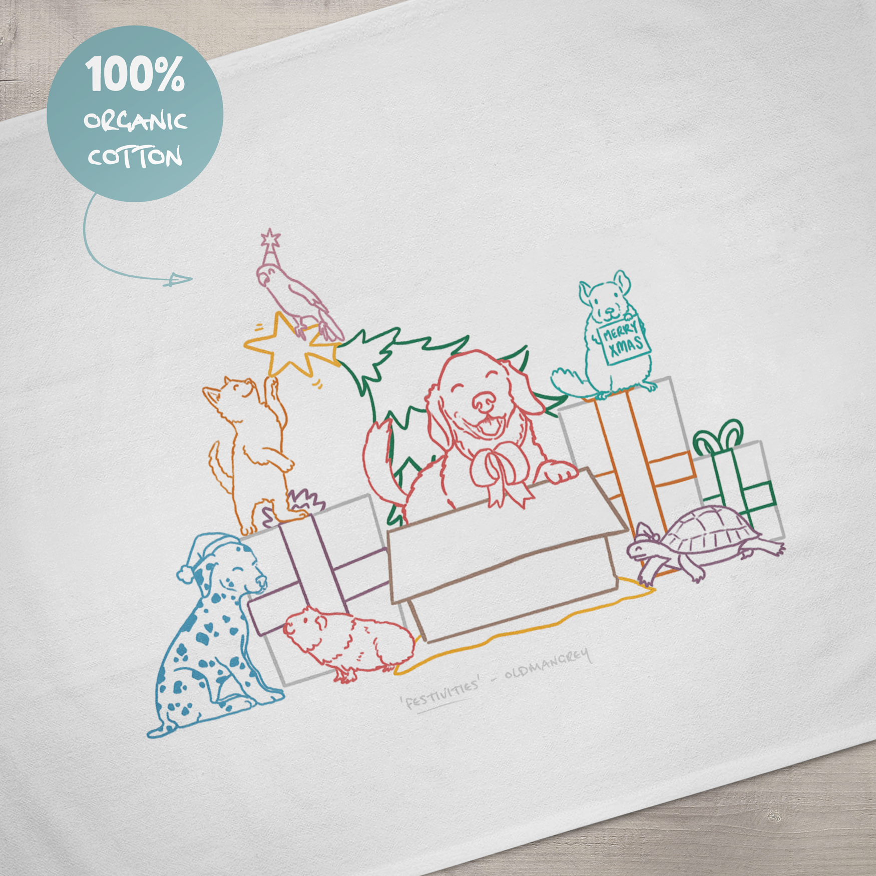 A close up of the design on a large tea towel. It has a colourful digital illustration of 7 pets opening Christmas presents & playing with the Christmas tree! A sign says '100% organic cotton'.