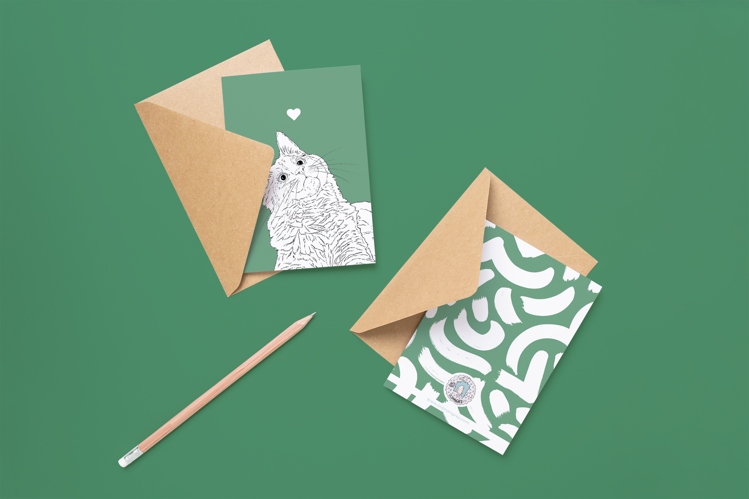 Two cards on brown envelopes, one face up one down. The card and image have a green coloured background, with a black & white digital illustration of the head & shoulders of a Kitty Cat.