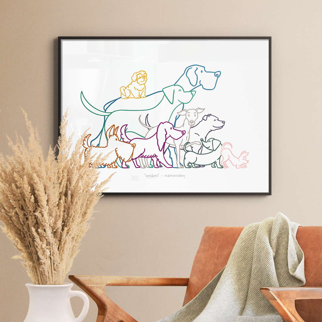 An A3 print in a thin dark frame on a white wall with soft light. A chair & dried flowers are in the foreground. The print has a colourful digital illustration of 9 dogs all ready to go walkies!