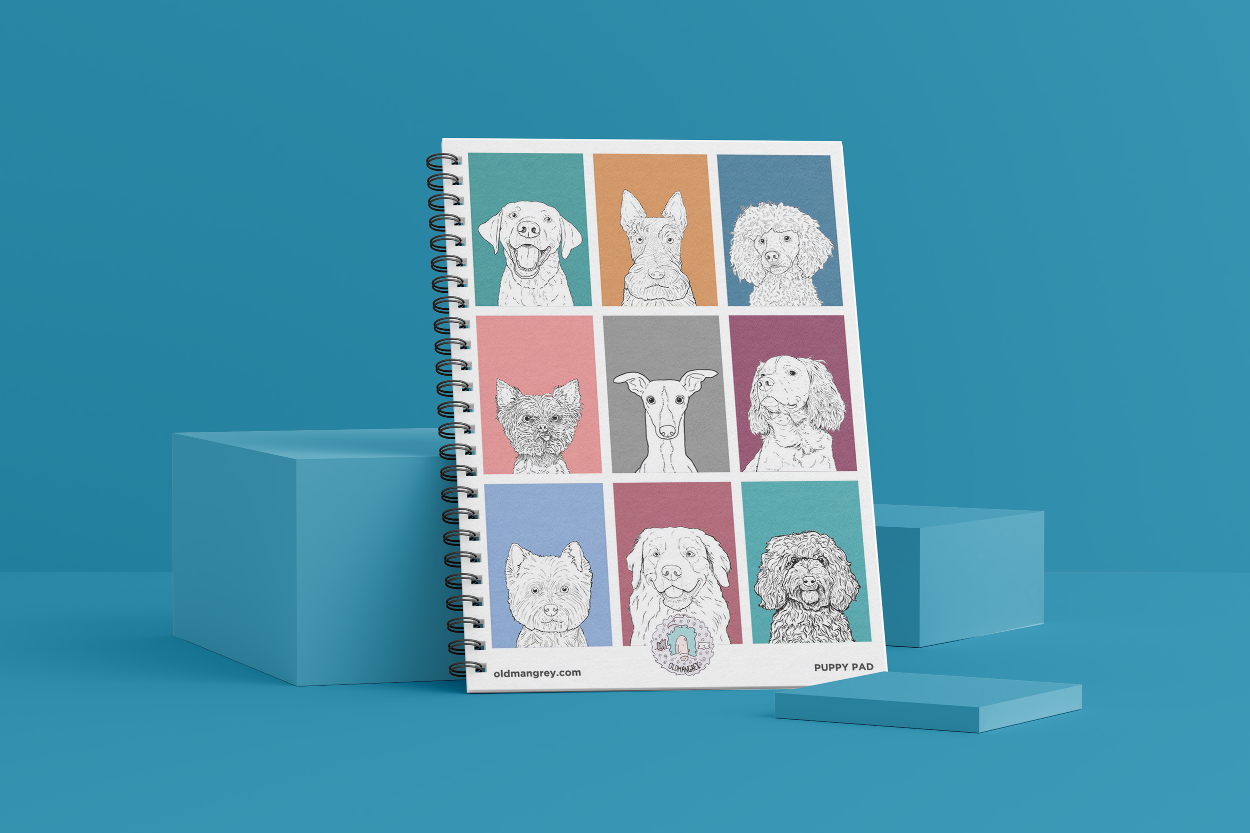 My A5 Puppy Pad wire bound notebook against a blue backdrop. It has 9 brightly coloured boxes each with a black & white digital illustration of the head & shoulders of different dog breeds.