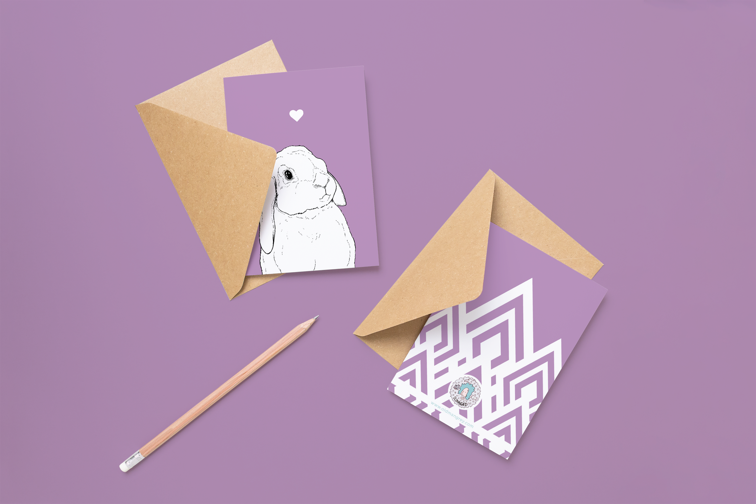 Two cards on brown envelopes, one face up one down. The card and image have a lilac purple coloured background, with a black & white digital illustration of the head & shoulders of a Lop Eared Bunny.
