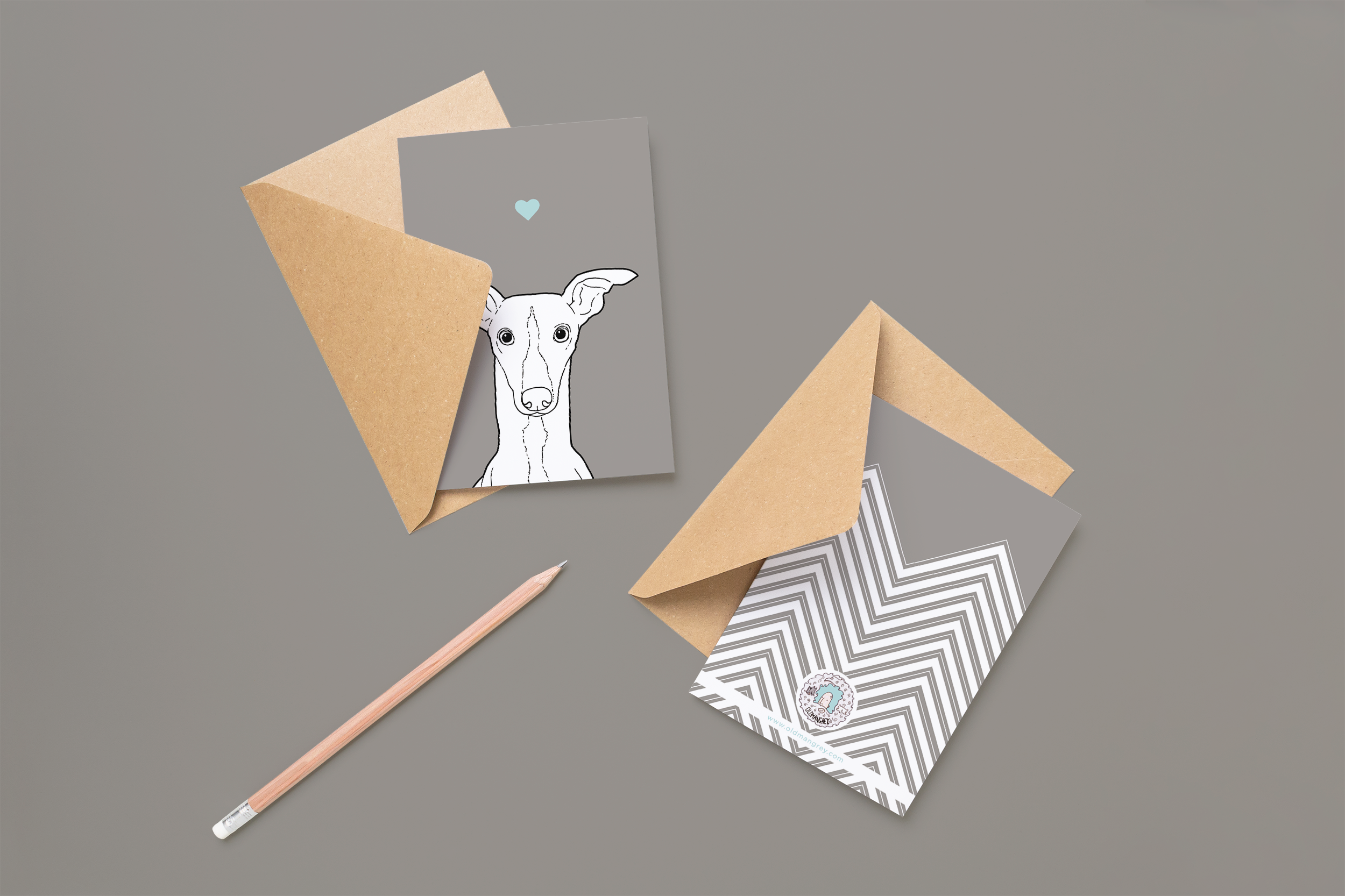 Two cards on brown envelopes, one face up one down. The card and image have a pale grey coloured background, with a black & white digital illustration of the head & shoulders of a Whippetdog.