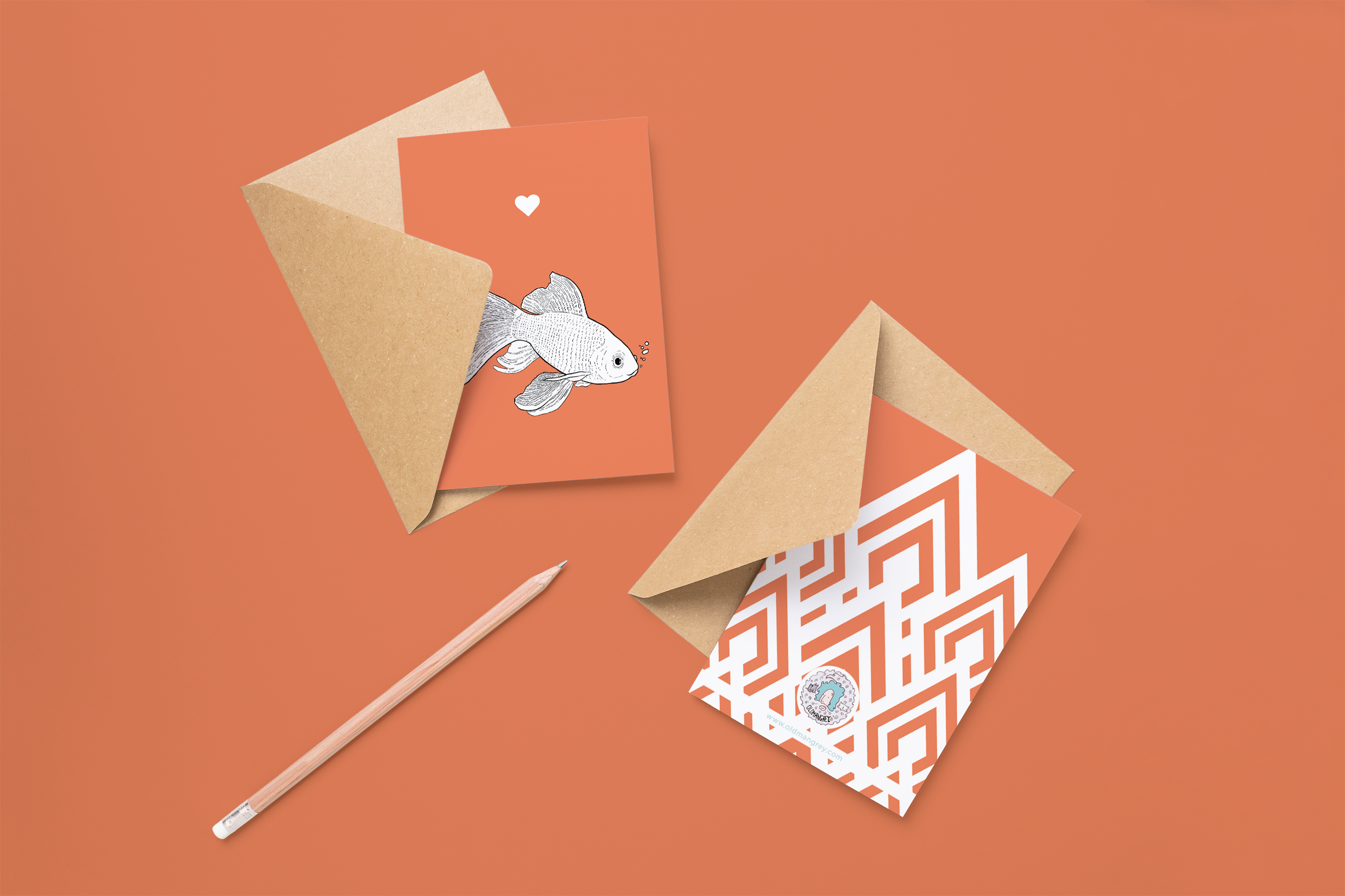 Two cards on brown envelopes, one face up one down. The card and image have a red coloured background, with a black & white digital illustration of a Goldfish.