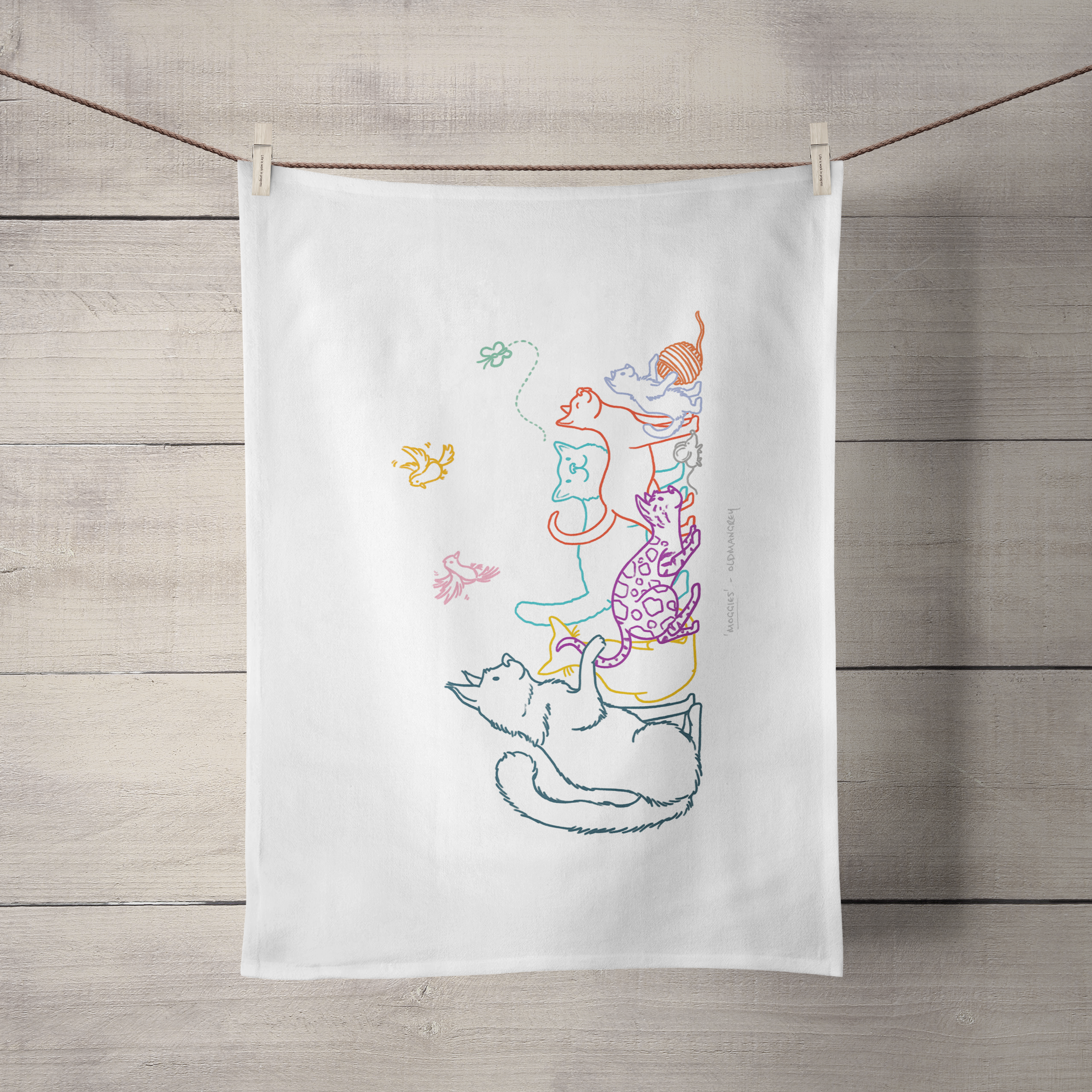 A large tea towel hanging by its short side from a piece of string. It has a colourful digital illustration of 6 cats, 2 birds, a butterfly & mouse.