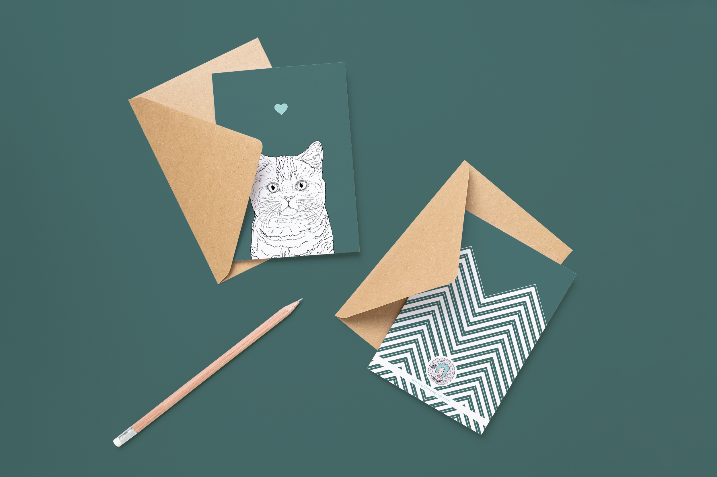 Two cards on brown envelopes, one face up one down. The card and image have a deep green coloured background, with a black & white digital illustration of the head & shoulders of a stripy Moggy.
