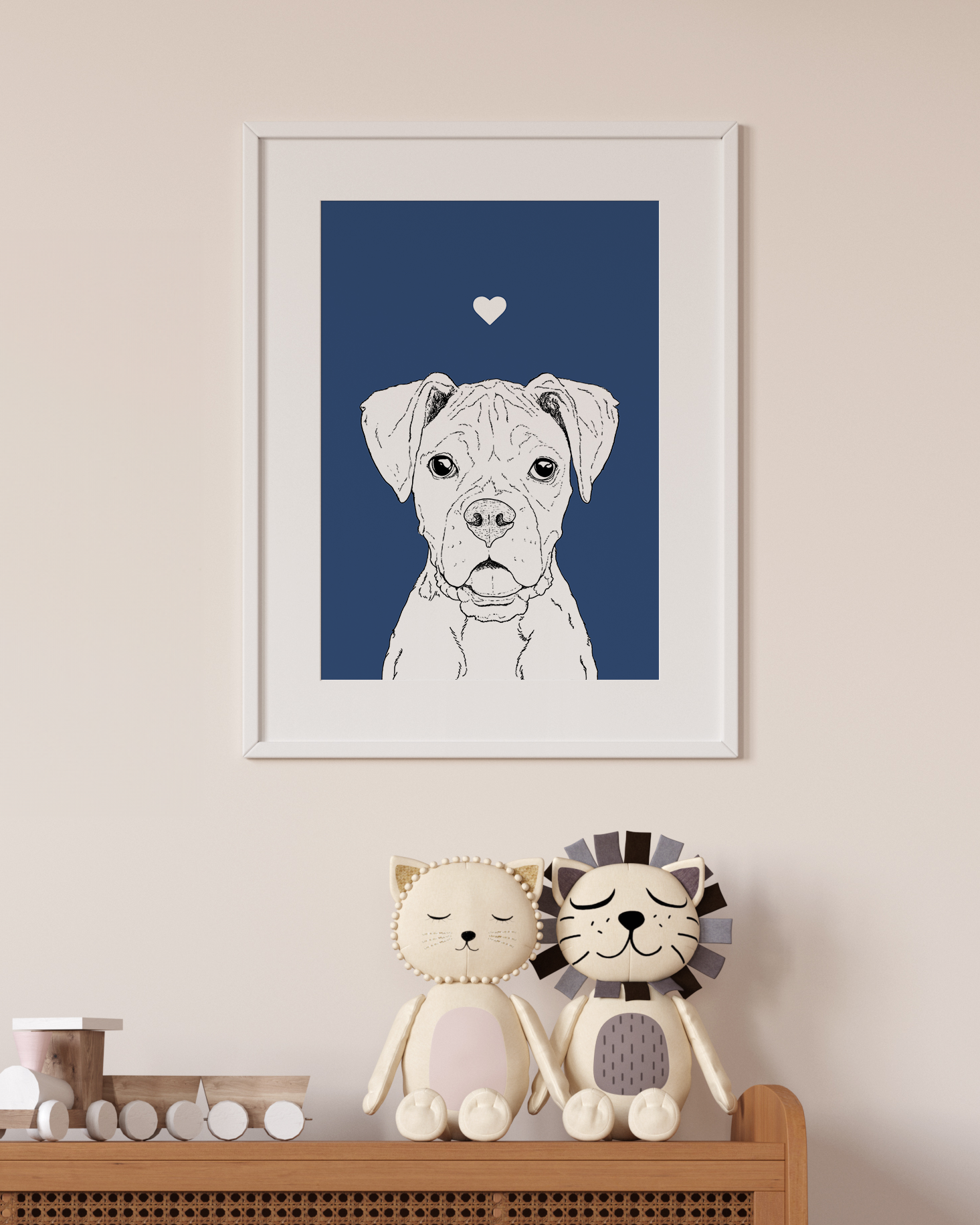 An A4 print in a white frame on a wall above 2 lion toys sitting on a unit. It has a black & white illustration of the head & shoulders of a Boxer dog on a navy blue background.